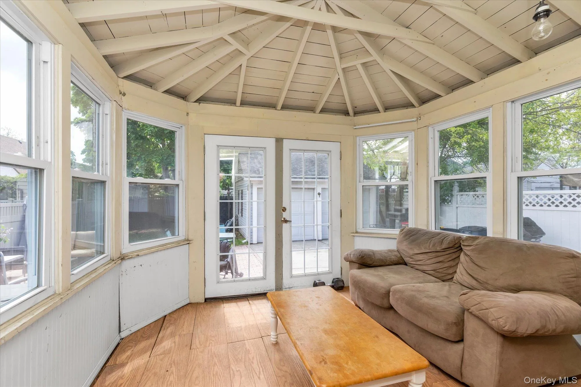 Sunroom featuring multiple windows, a multi-faceted ceiling, wood-finish flooring, and a pair of French doors providing exterior access Sunroom featuring multiple windows, a multi-faceted ceiling, wood-finish flooring, and a pair of French doors providing exterior access