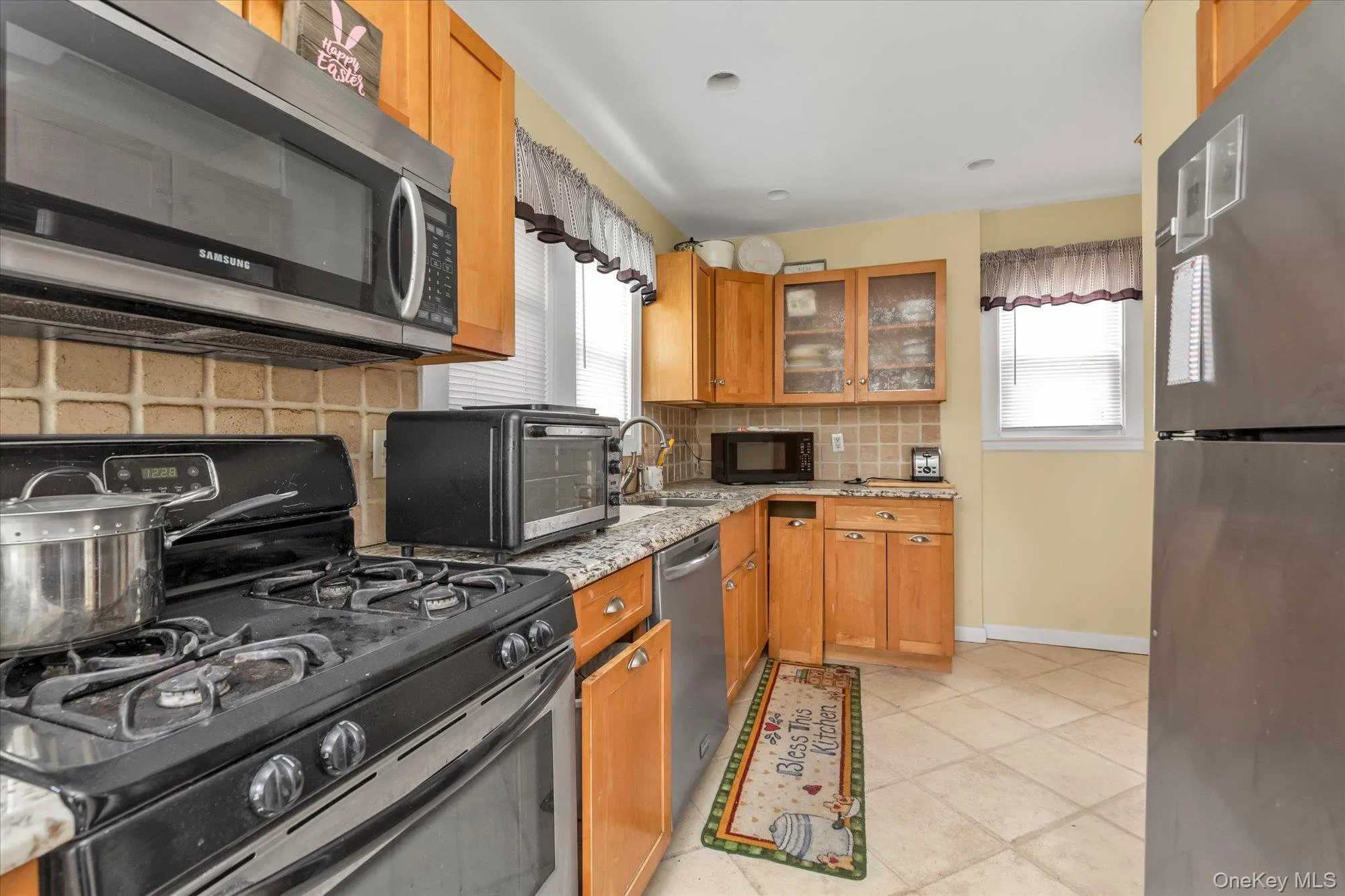 Kitchen featuring wood-finish cabinetry, stainless steel appliances, granite-style countertops, and a ceramic tile backsplash Kitchen featuring wood-finish cabinetry, stainless steel appliances, granite-style countertops, and a ceramic tile backsplash