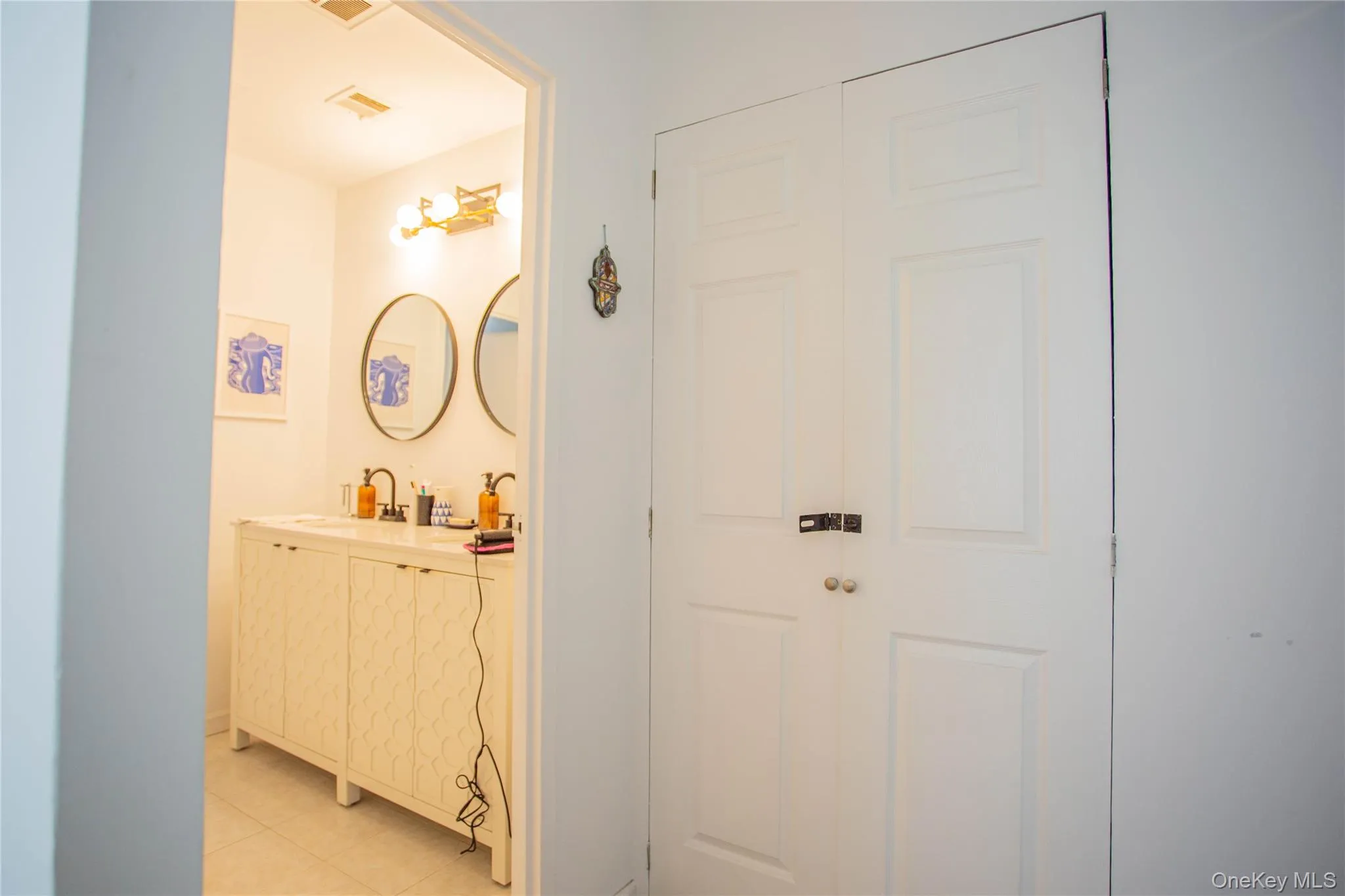 Hallway with light tile patterned floors, visible vents, and a sink Hallway with light tile patterned floors, visible vents, and a sink