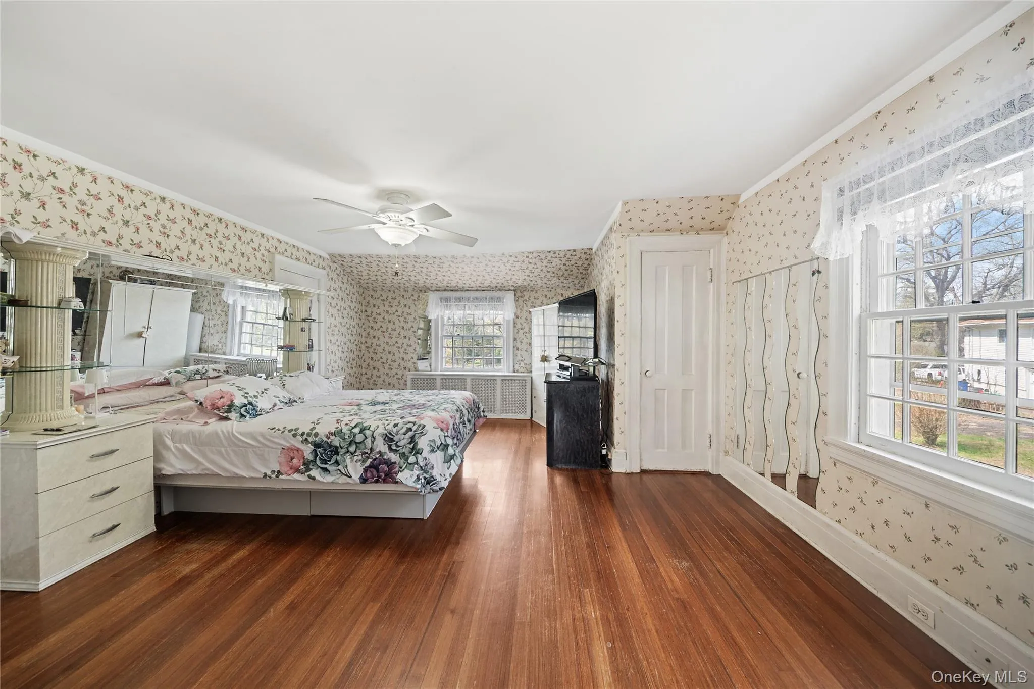 Hardwood flooring in a bright room featuring multiple windows, a ceiling fan, and a white paneled door Hardwood flooring in a bright room featuring multiple windows, a ceiling fan, and a white paneled door