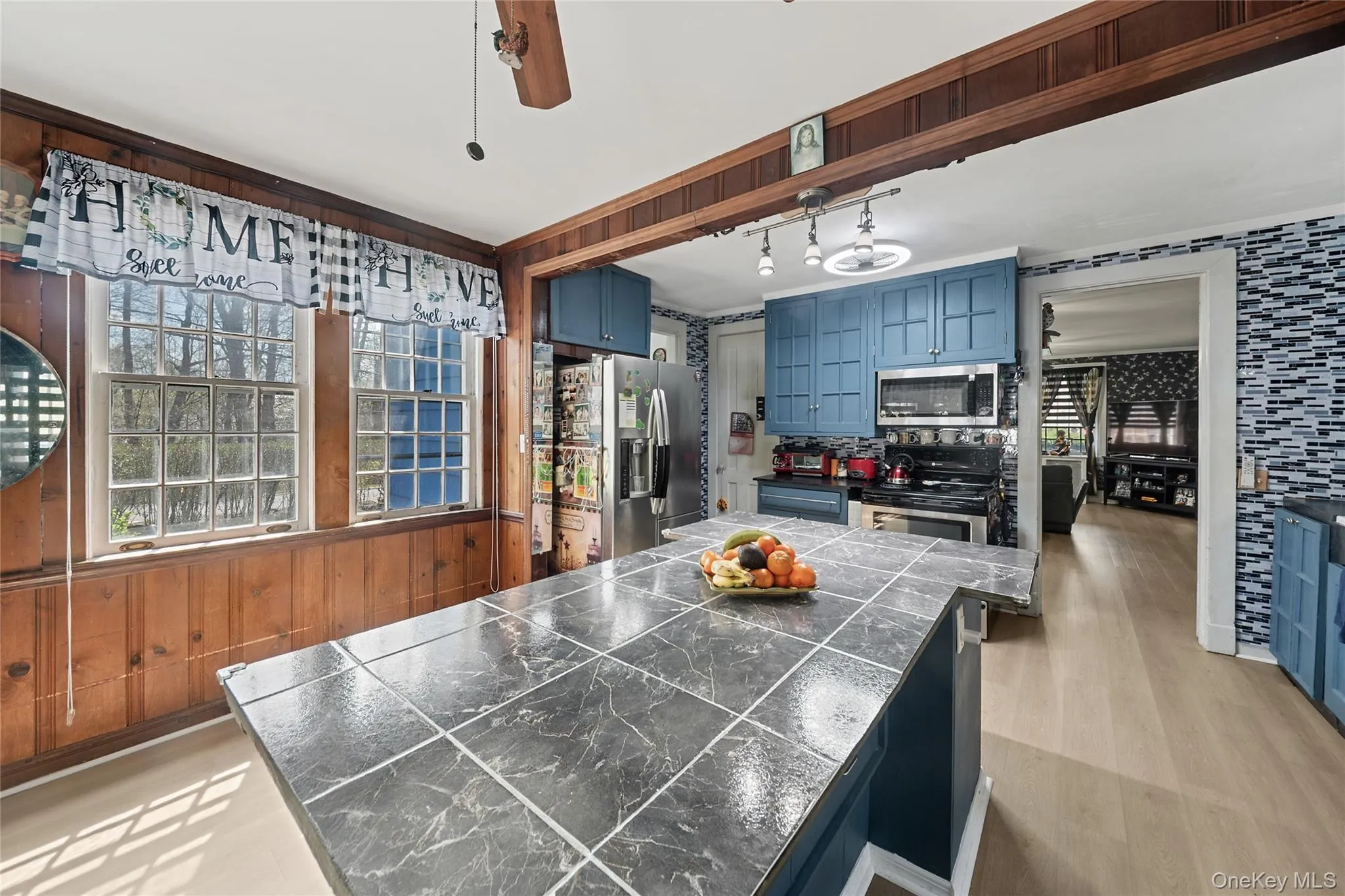 Kitchen featuring a large island with tiled countertop, blue cabinetry, stainless steel appliances, and light wood-finish flooring Kitchen featuring a large island with tiled countertop, blue cabinetry, stainless steel appliances, and light wood-finish flooring