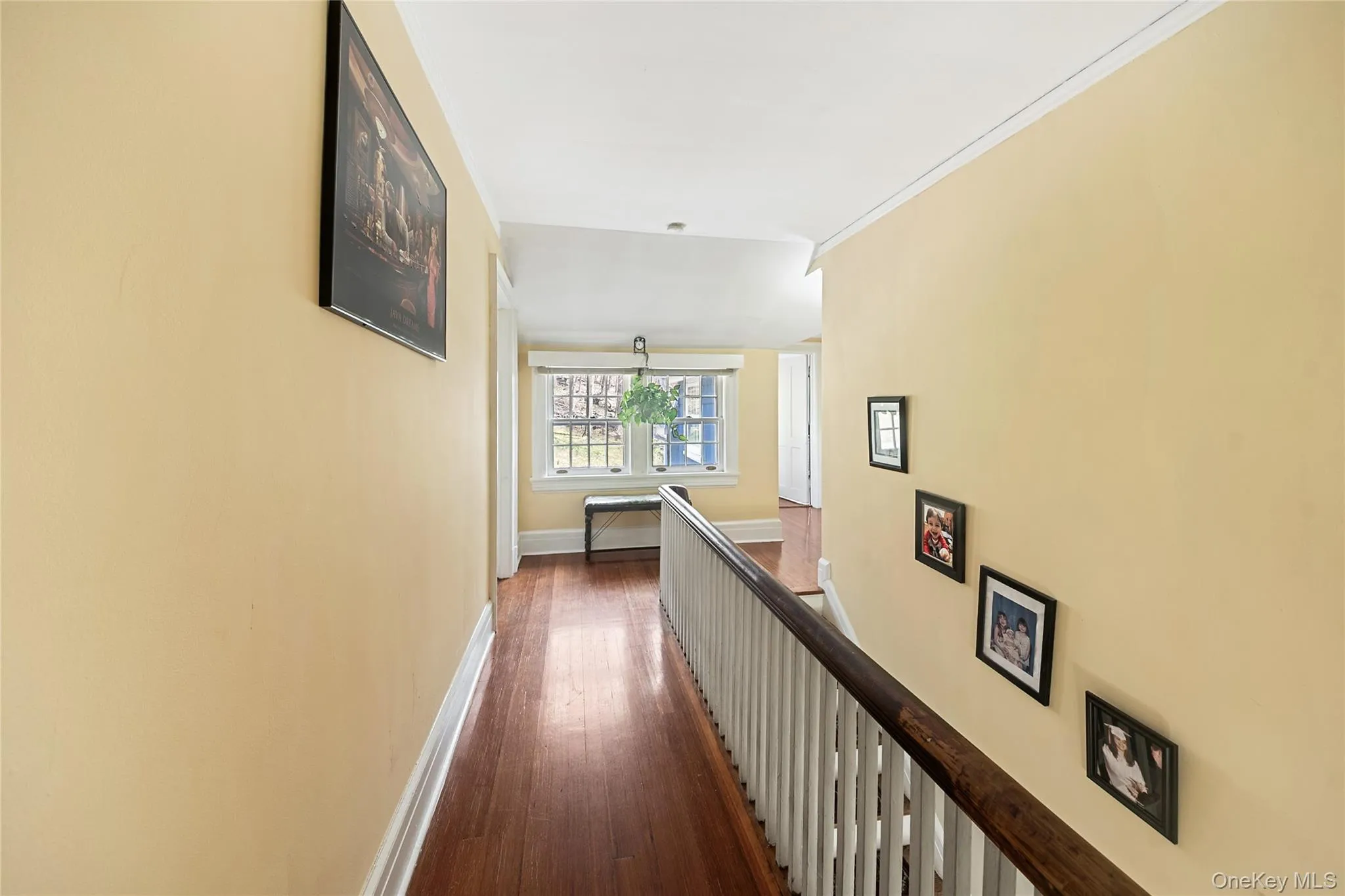 Hallway featuring wood-finish flooring, white crown molding, a white spindle railing, and a window with multiple panes Hallway featuring wood-finish flooring, white crown molding, a white spindle railing, and a window with multiple panes