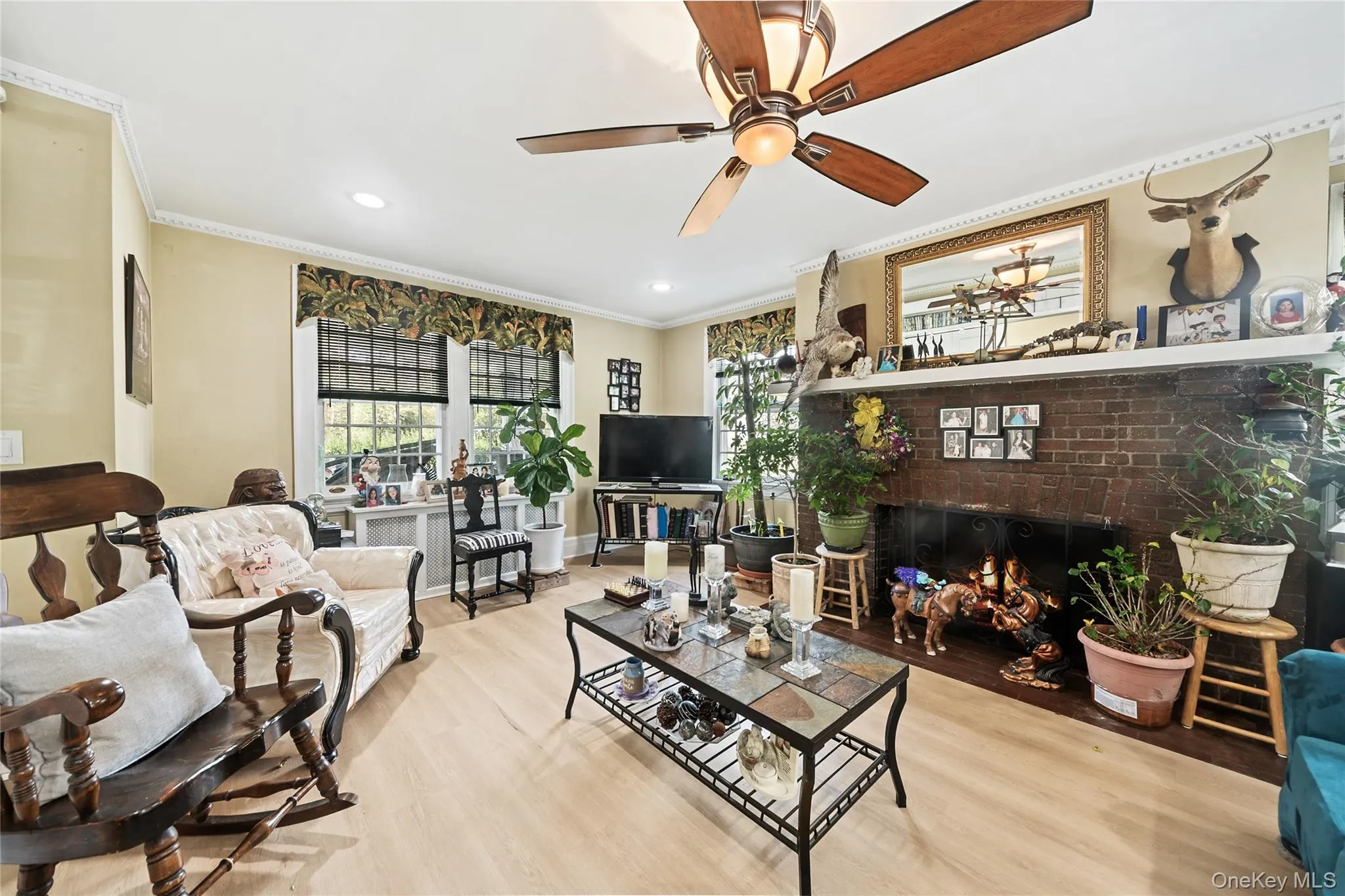 Spacious living area featuring light wood-finish flooring, a ceiling fan with integrated lighting, and crown molding Spacious living area featuring light wood-finish flooring, a ceiling fan with integrated lighting, and crown molding