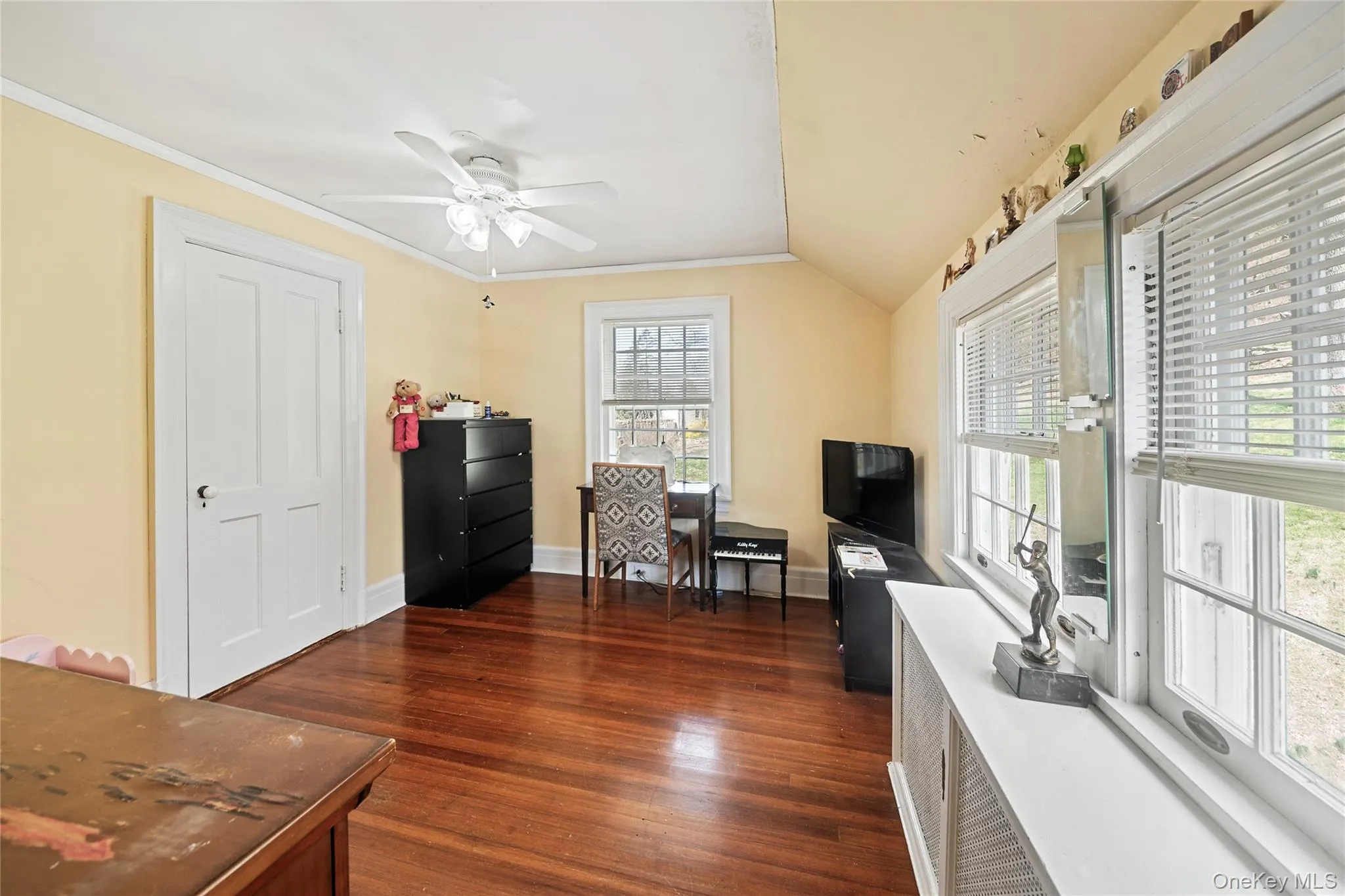 Hardwood flooring throughout featuring a ceiling fan, two windows with white blinds, a two-panel interior door, and a built-in window ledge Hardwood flooring throughout featuring a ceiling fan, two windows with white blinds, a two-panel interior door, and a built-in window ledge