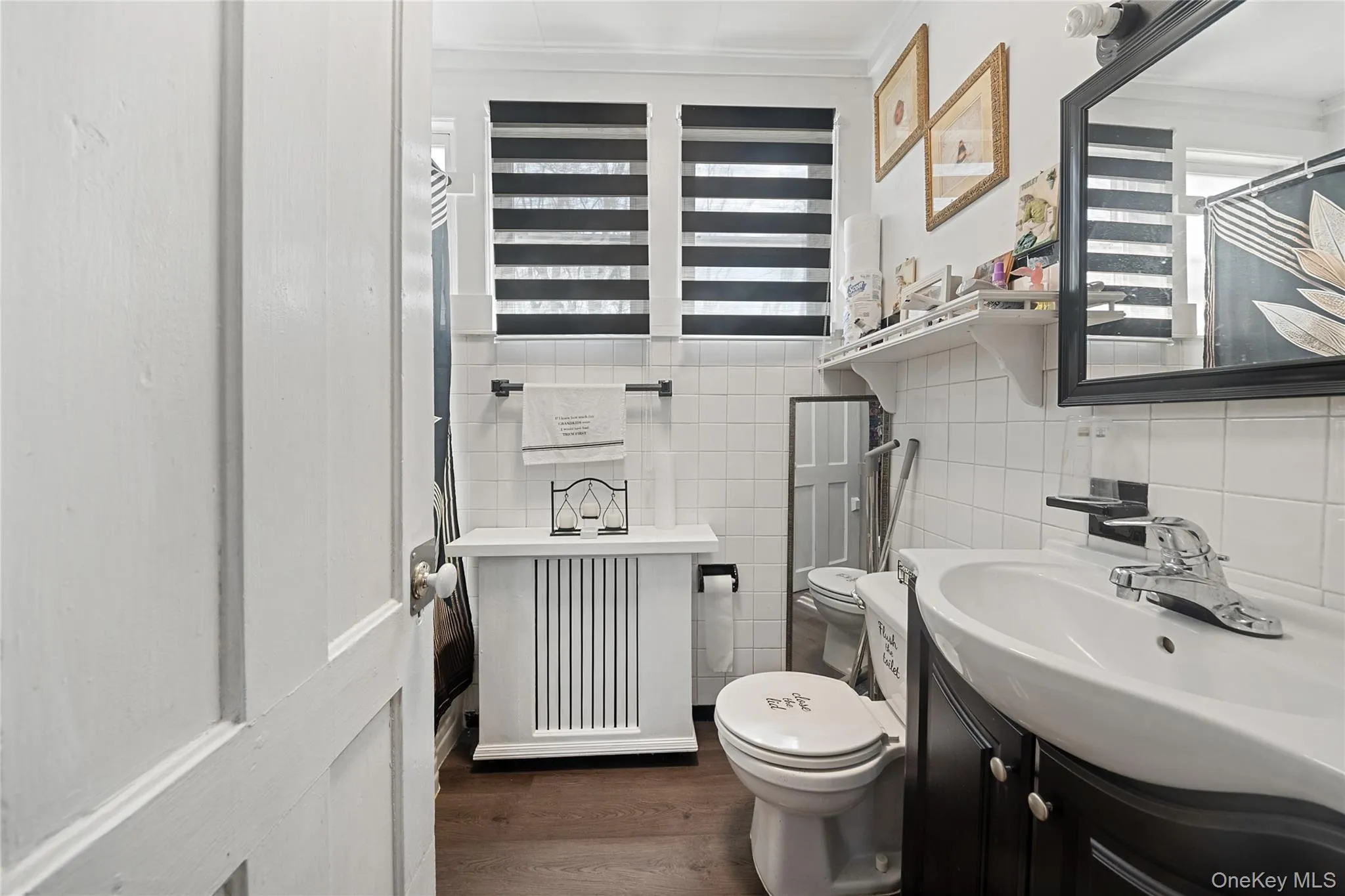 Bathroom featuring a dark wood-finish floor, white subway tile walls, and a dark wood vanity with a white basin sink Bathroom featuring a dark wood-finish floor, white subway tile walls, and a dark wood vanity with a white basin sink