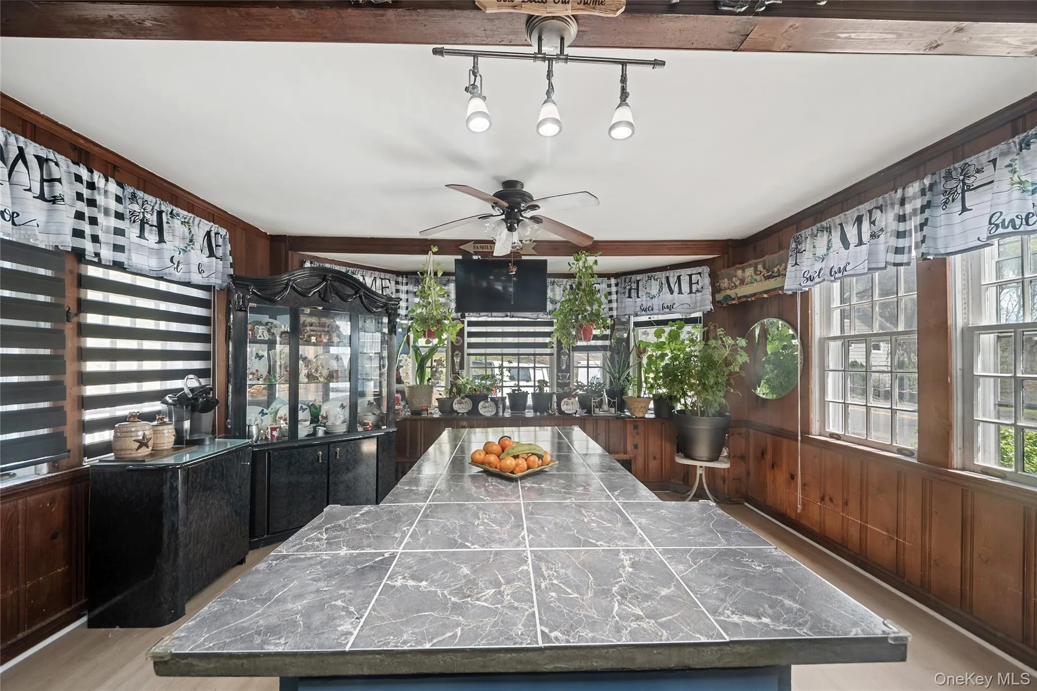 Spacious kitchen featuring a large central island with a tiled countertop, natural wood paneling, multiple windows, exposed ceiling beams, and recessed lighting Spacious kitchen featuring a large central island with a tiled countertop, natural wood paneling, multiple windows, exposed ceiling beams, and recessed lighting