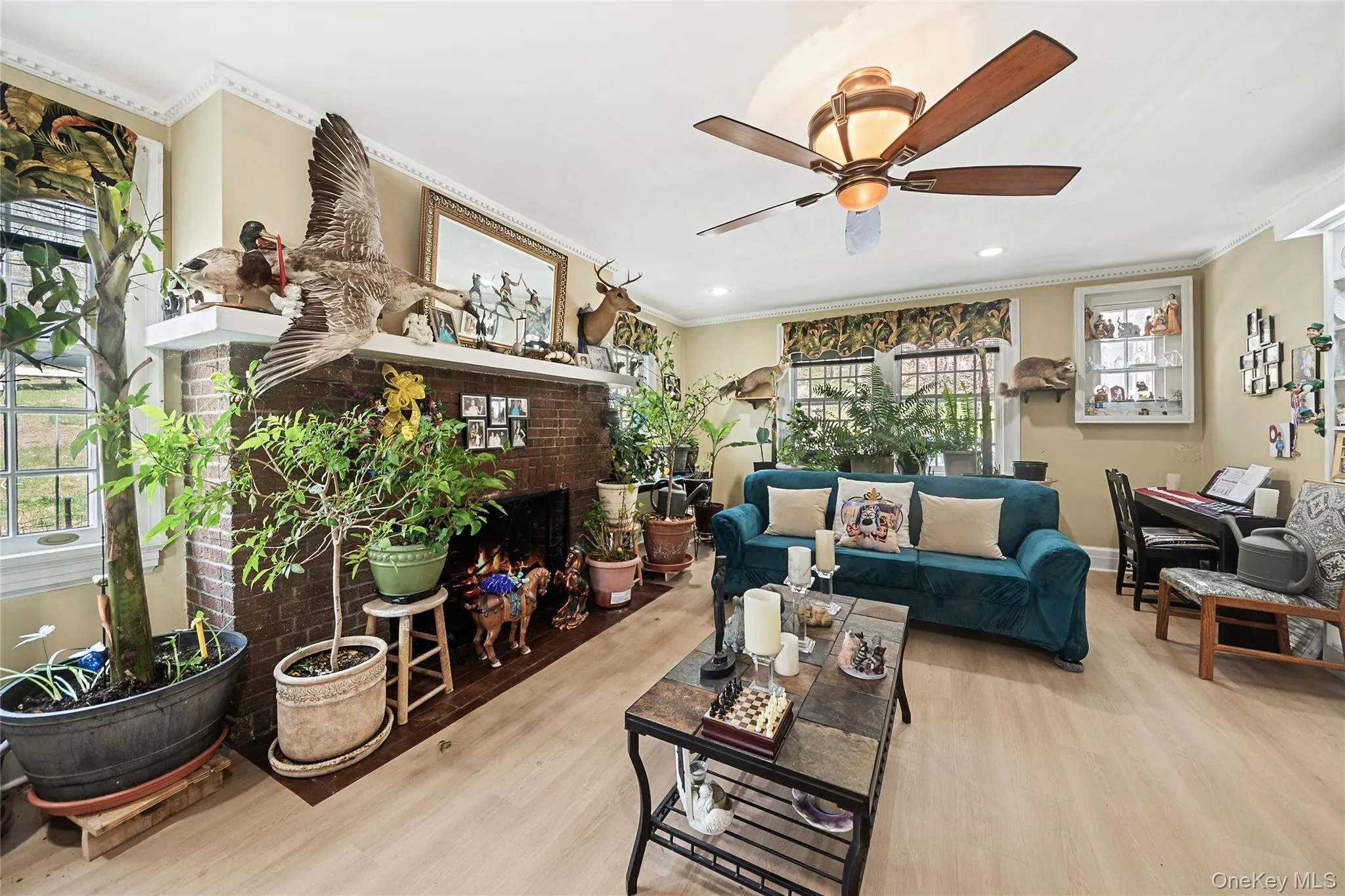 Spacious interior featuring wood-finish flooring, a brick fireplace with a white mantel, and crown molding Spacious interior featuring wood-finish flooring, a brick fireplace with a white mantel, and crown molding