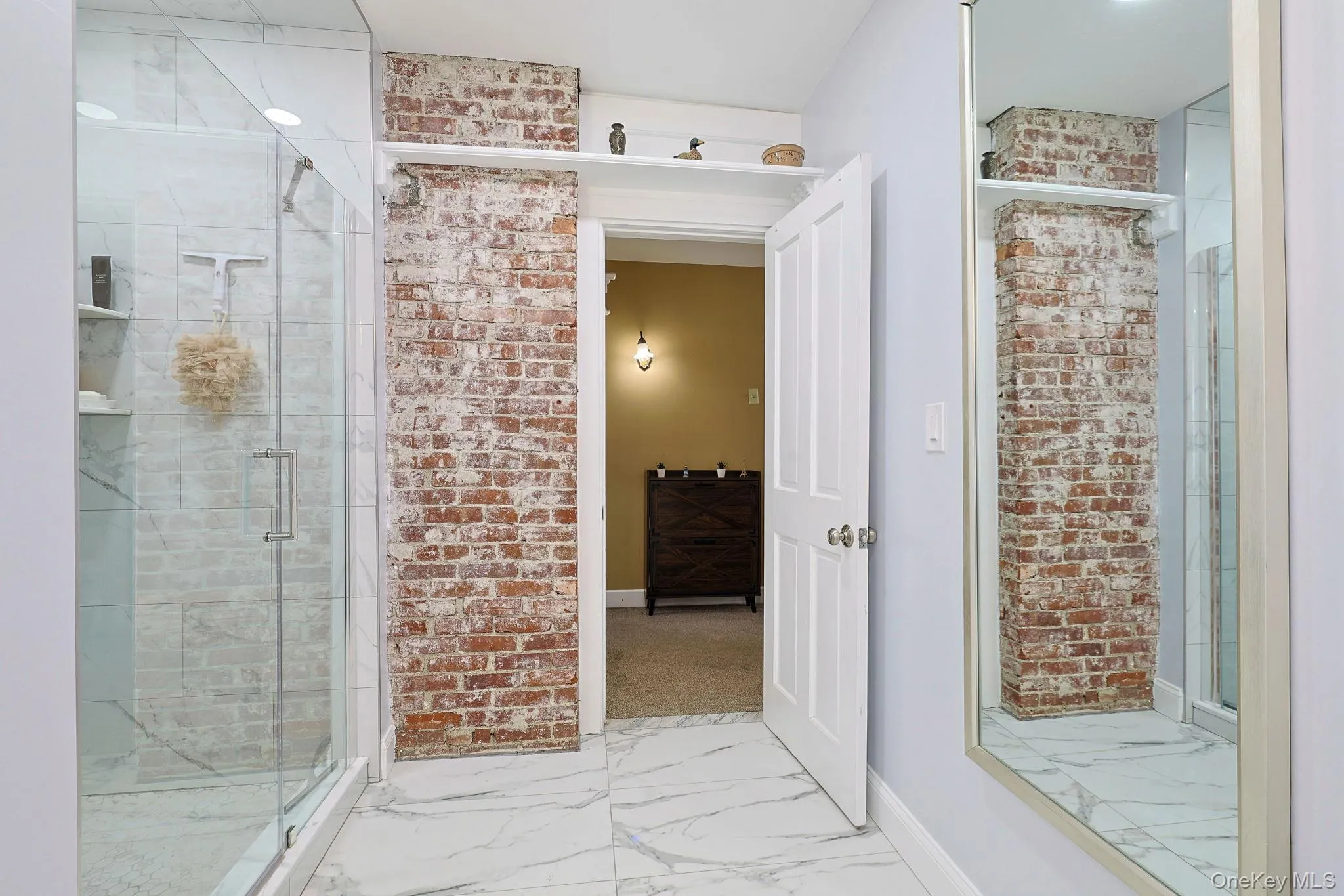 Modern bathroom with white marble-look tile flooring, a clear glass shower enclosure, and an exposed brick feature wall Modern bathroom with white marble-look tile flooring, a clear glass shower enclosure, and an exposed brick feature wall