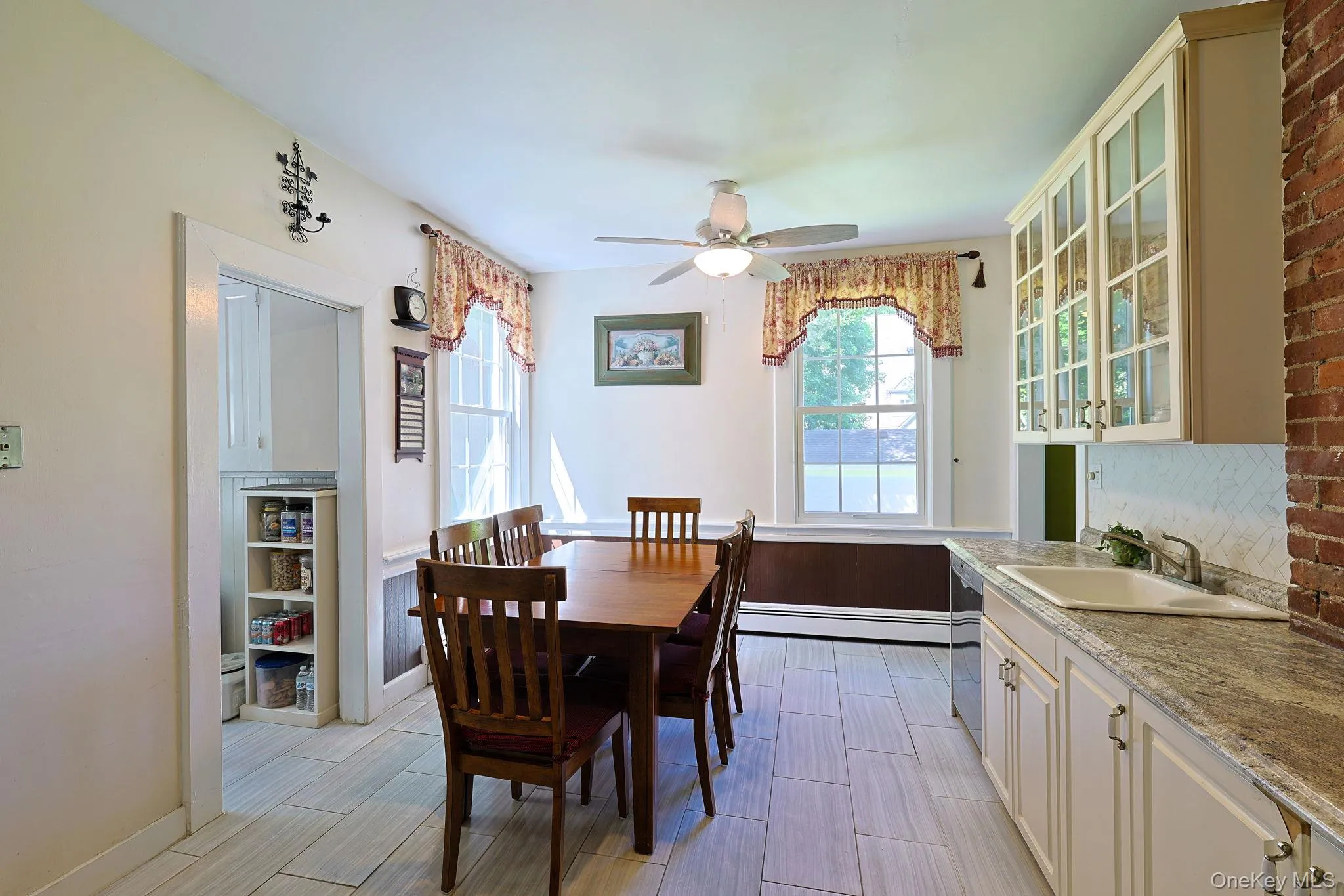 Kitchen and dining area featuring light-toned tile flooring, white cabinetry with glass-front uppers, a light-colored countertop, and a built-in sink with a stainless steel faucet Kitchen and dining area featuring light-toned tile flooring, white cabinetry with glass-front uppers, a light-colored countertop, and a built-in sink with a stainless steel faucet