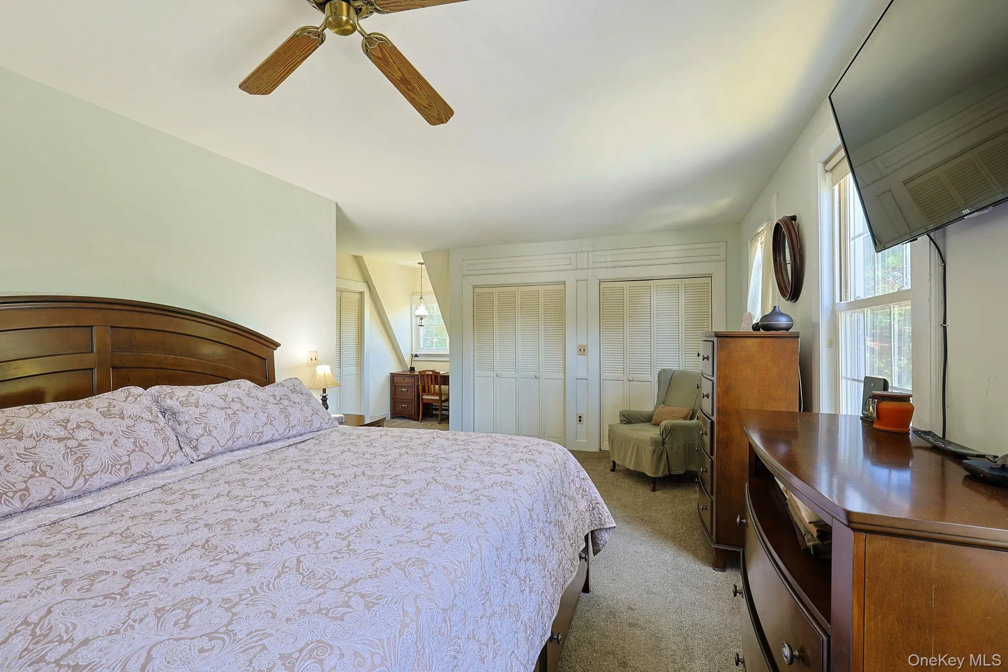 Spacious Primary bedroom with a wood-finish ceiling fan, neutral carpet, and multiple windows providing natural light Spacious Primary bedroom with a wood-finish ceiling fan, neutral carpet, and multiple windows providing natural light