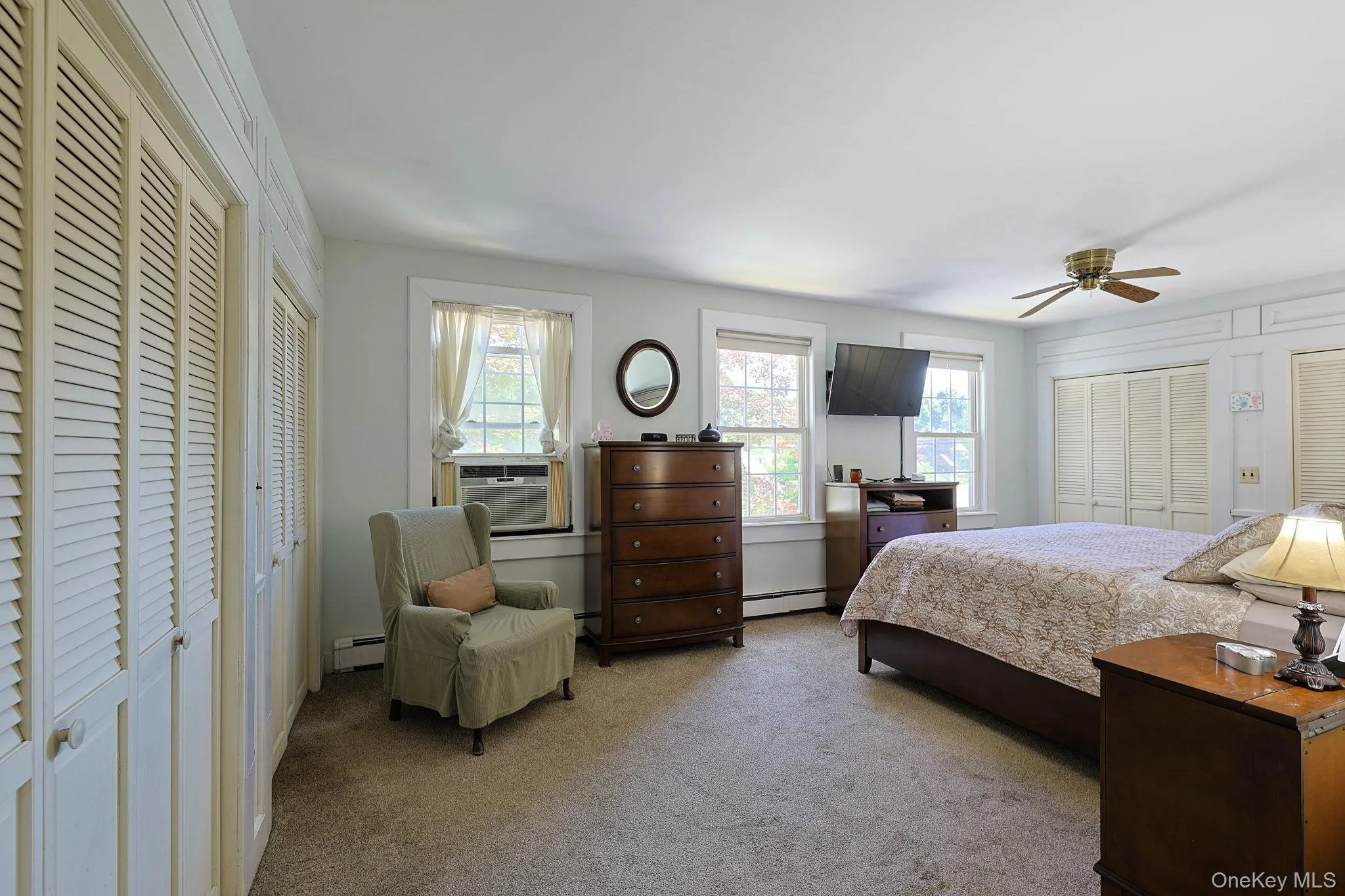Carpeted room Primary bedroom featuring multiple windows with natural light, two sets of louvered bi-fold doors, and a ceiling fan Carpeted room Primary bedroom featuring multiple windows with natural light, two sets of louvered bi-fold doors, and a ceiling fan