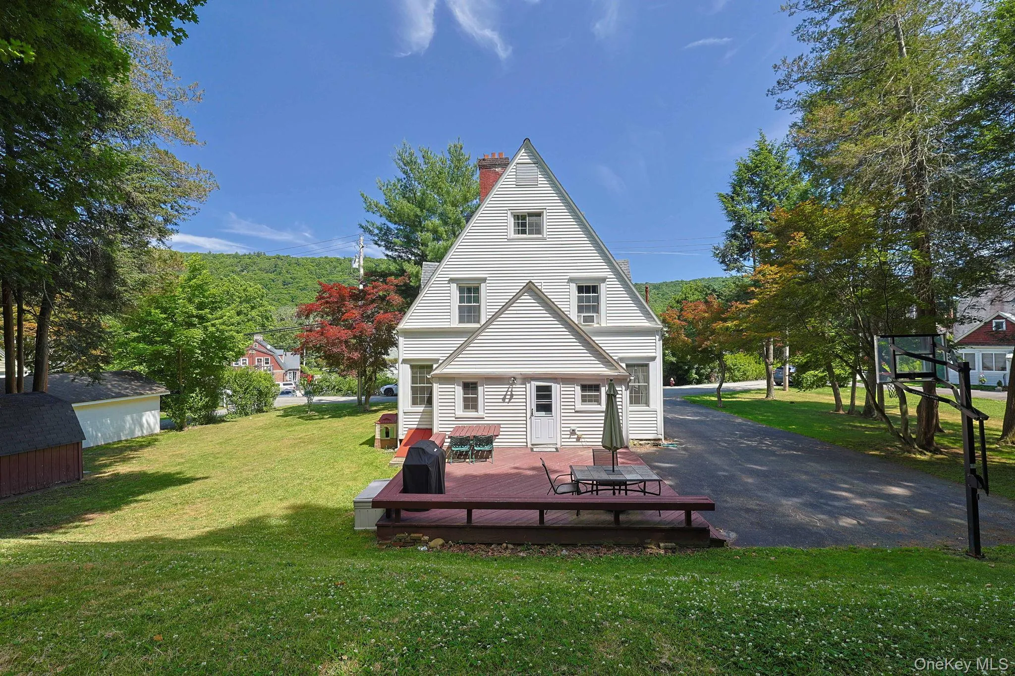 Rear exterior with a spacious wood-finish deck, white siding, and a prominent red brick chimney Rear exterior with a spacious wood-finish deck, white siding, and a prominent red brick chimney