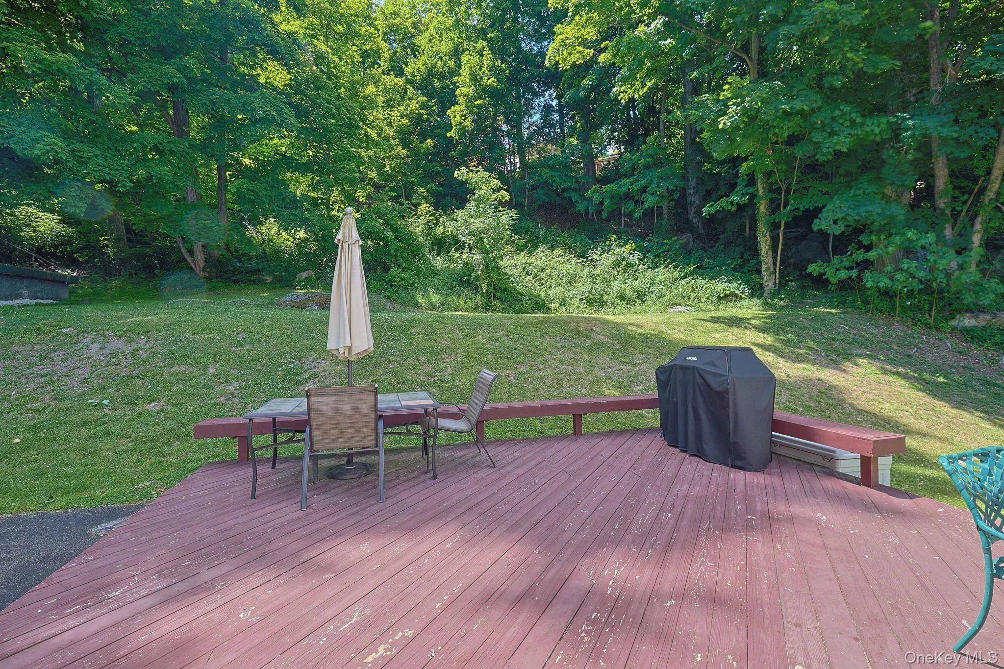 Expansive wood-finish deck with integrated bench seating, overlooking a sloped grassy area and mature trees Expansive wood-finish deck with integrated bench seating, overlooking a sloped grassy area and mature trees