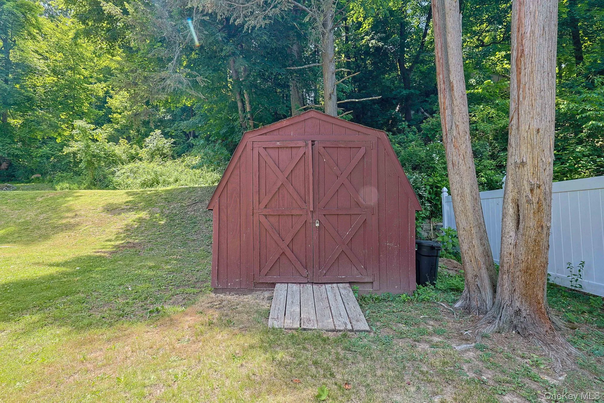 Red wood-sided shed with double barn doors, featuring a wood plank ramp entry Red wood-sided shed with double barn doors, featuring a wood plank ramp entry