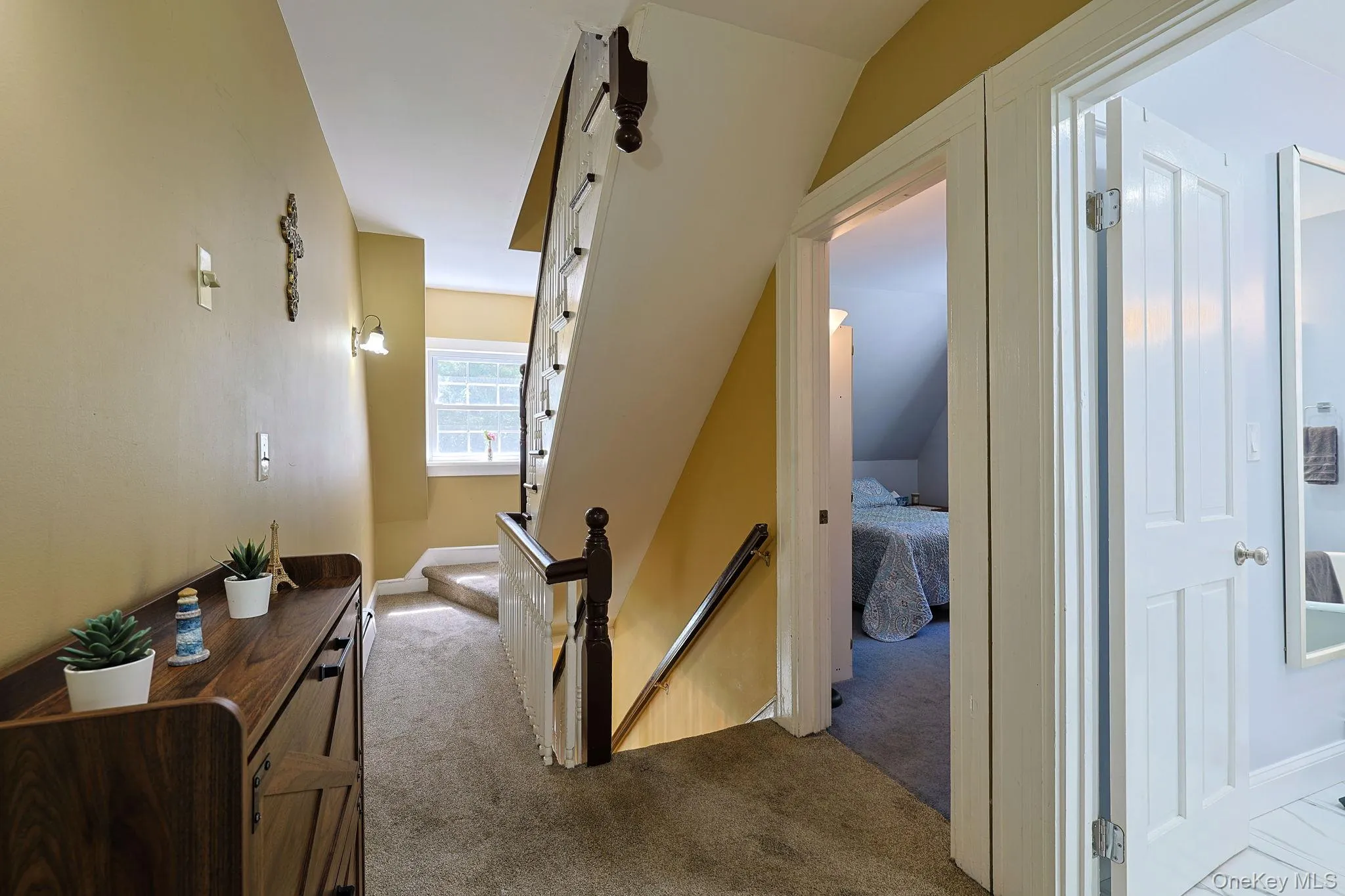 Carpeted hallway featuring a wood-finish console table, sconce lighting, and white trim Carpeted hallway featuring a wood-finish console table, sconce lighting, and white trim
