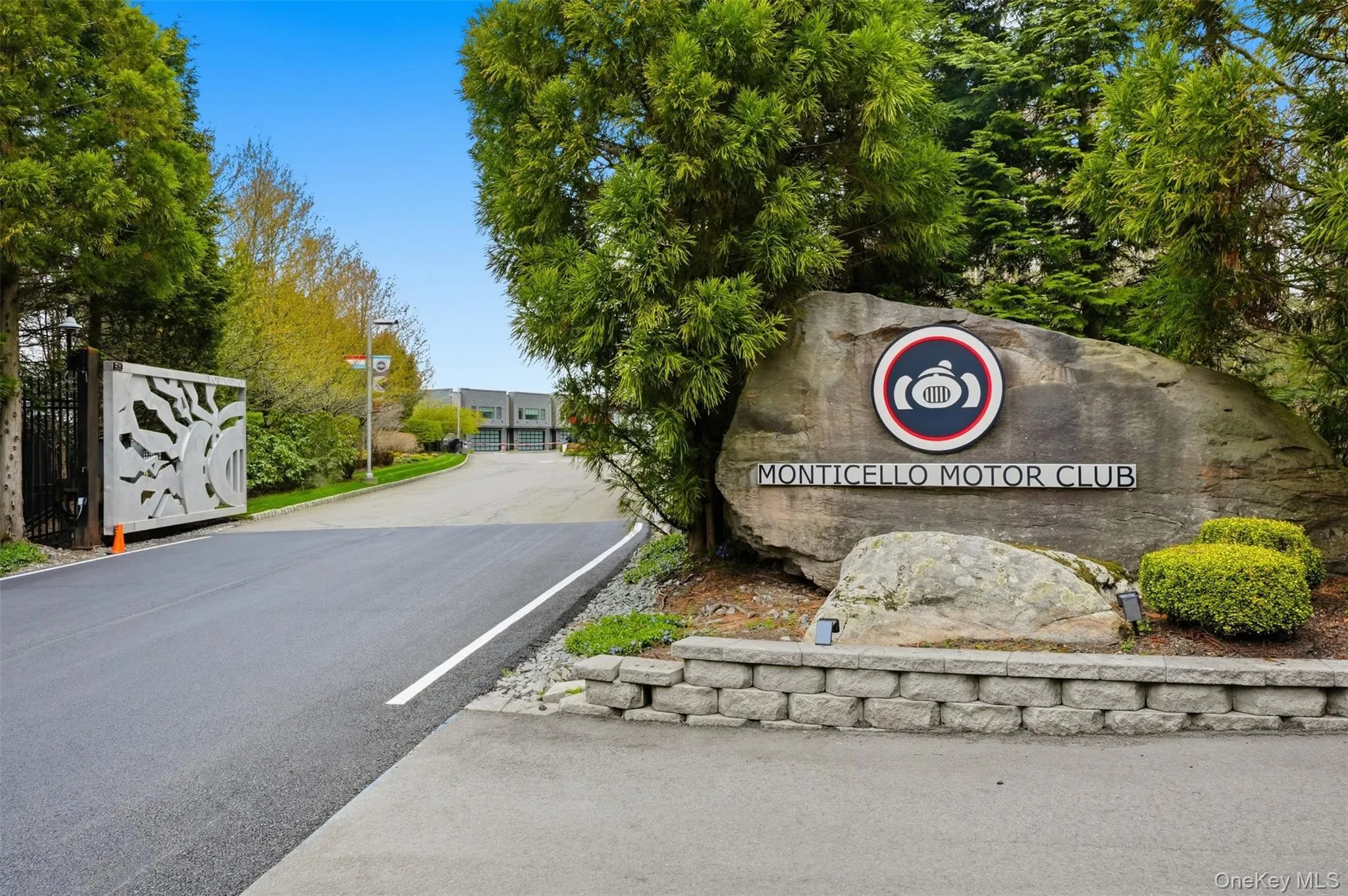 Entryway featuring a decorative metal gate, asphalt paving, and a stone monument sign Entryway featuring a decorative metal gate, asphalt paving, and a stone monument sign