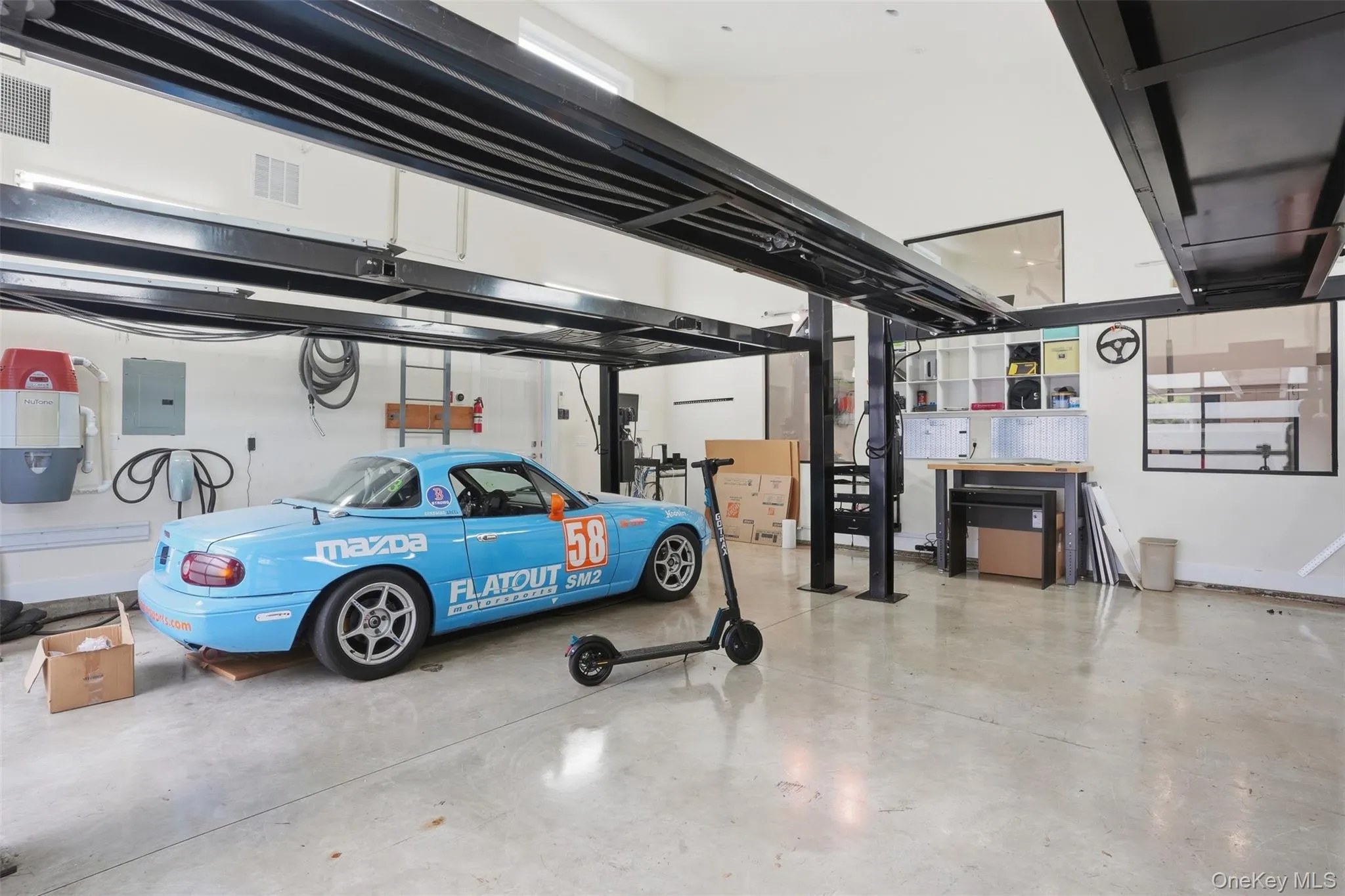 Spacious garage featuring a four-post car lift, polished concrete flooring, built-in shelving, and a dedicated workspace Spacious garage featuring a four-post car lift, polished concrete flooring, built-in shelving, and a dedicated workspace