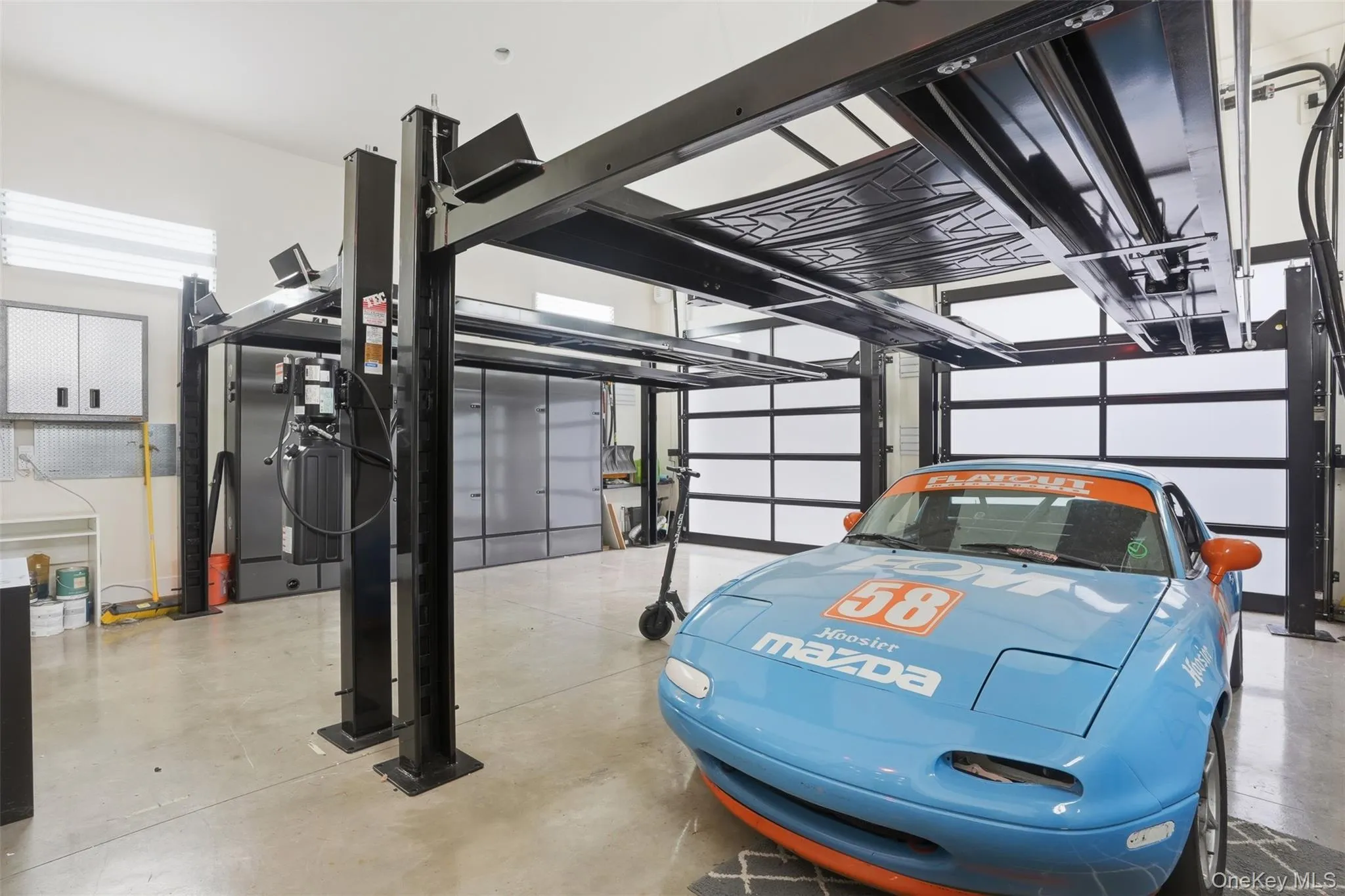 Spacious garage featuring a four-post car lift, polished concrete flooring, two overhead garage doors with frosted panels, and wall-mounted storage cabinetry Spacious garage featuring a four-post car lift, polished concrete flooring, two overhead garage doors with frosted panels, and wall-mounted storage cabinetry