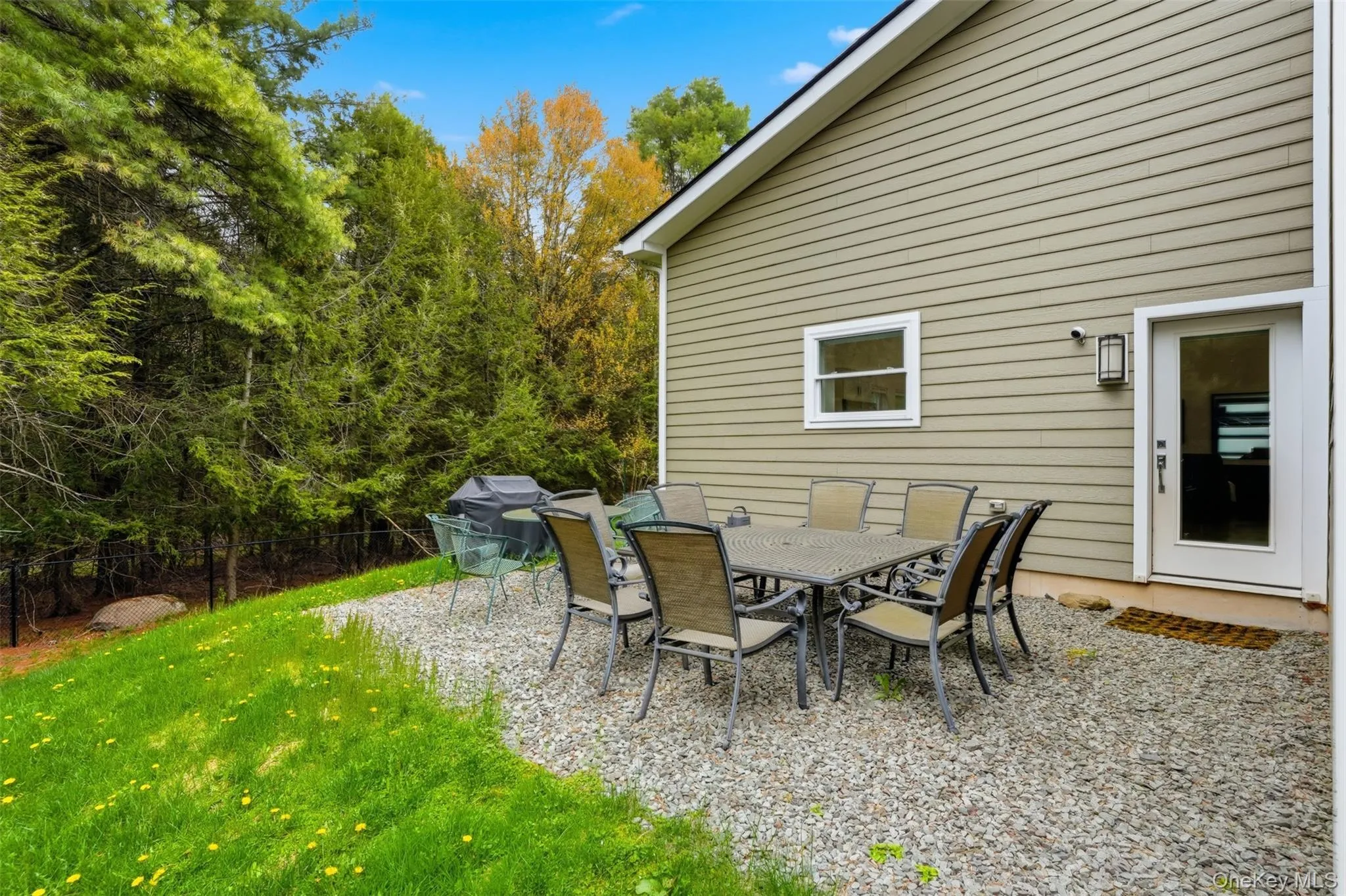 Outdoor patio space featuring a gravel surface, exterior wall with horizontal siding, and a white framed door with a glass panel Outdoor patio space featuring a gravel surface, exterior wall with horizontal siding, and a white framed door with a glass panel