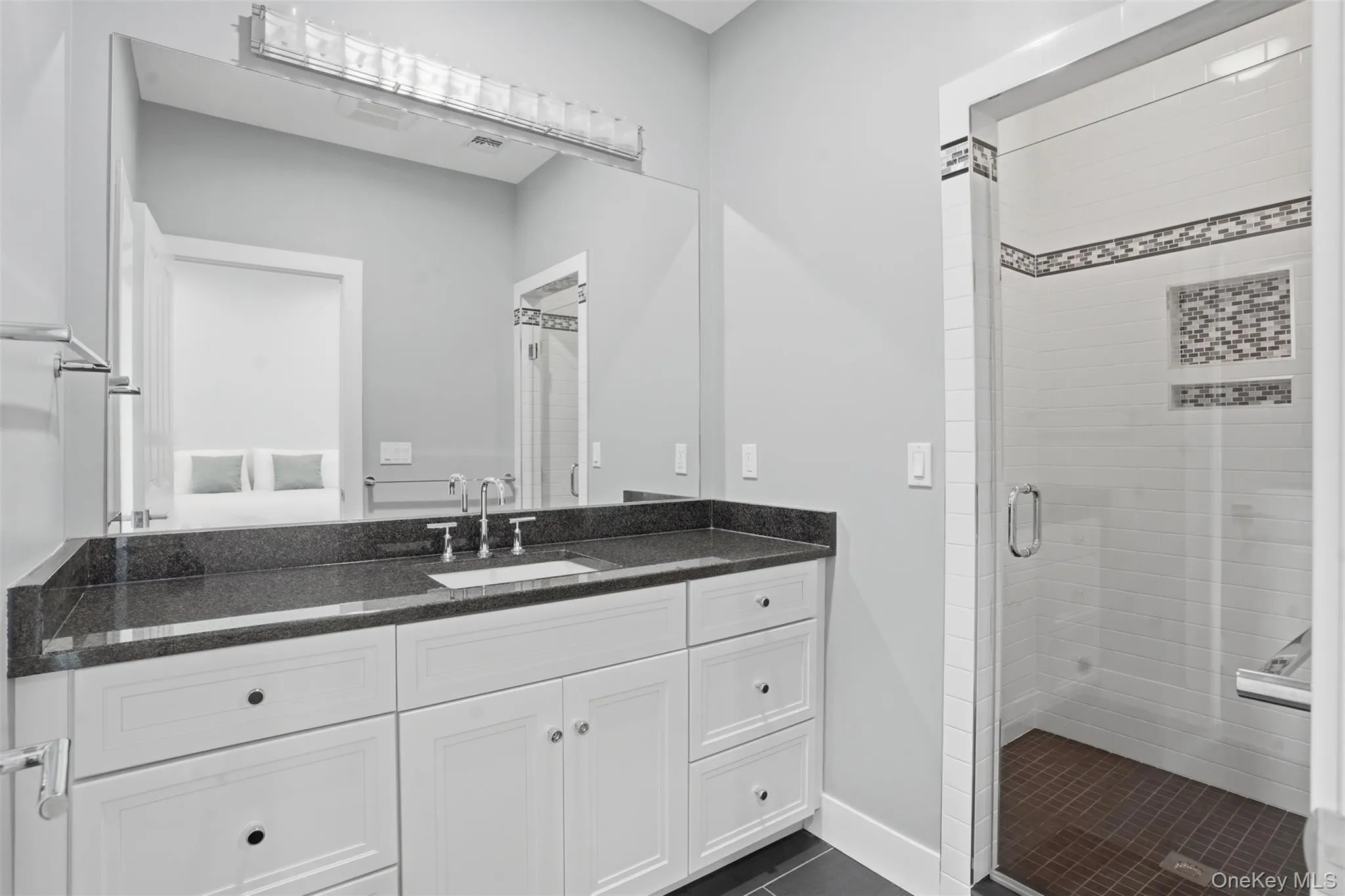 Bathroom featuring an expansive vanity with a dark countertop and undermount sink, white cabinetry with dark hardware, and a large wall-mounted mirror Bathroom featuring an expansive vanity with a dark countertop and undermount sink, white cabinetry with dark hardware, and a large wall-mounted mirror