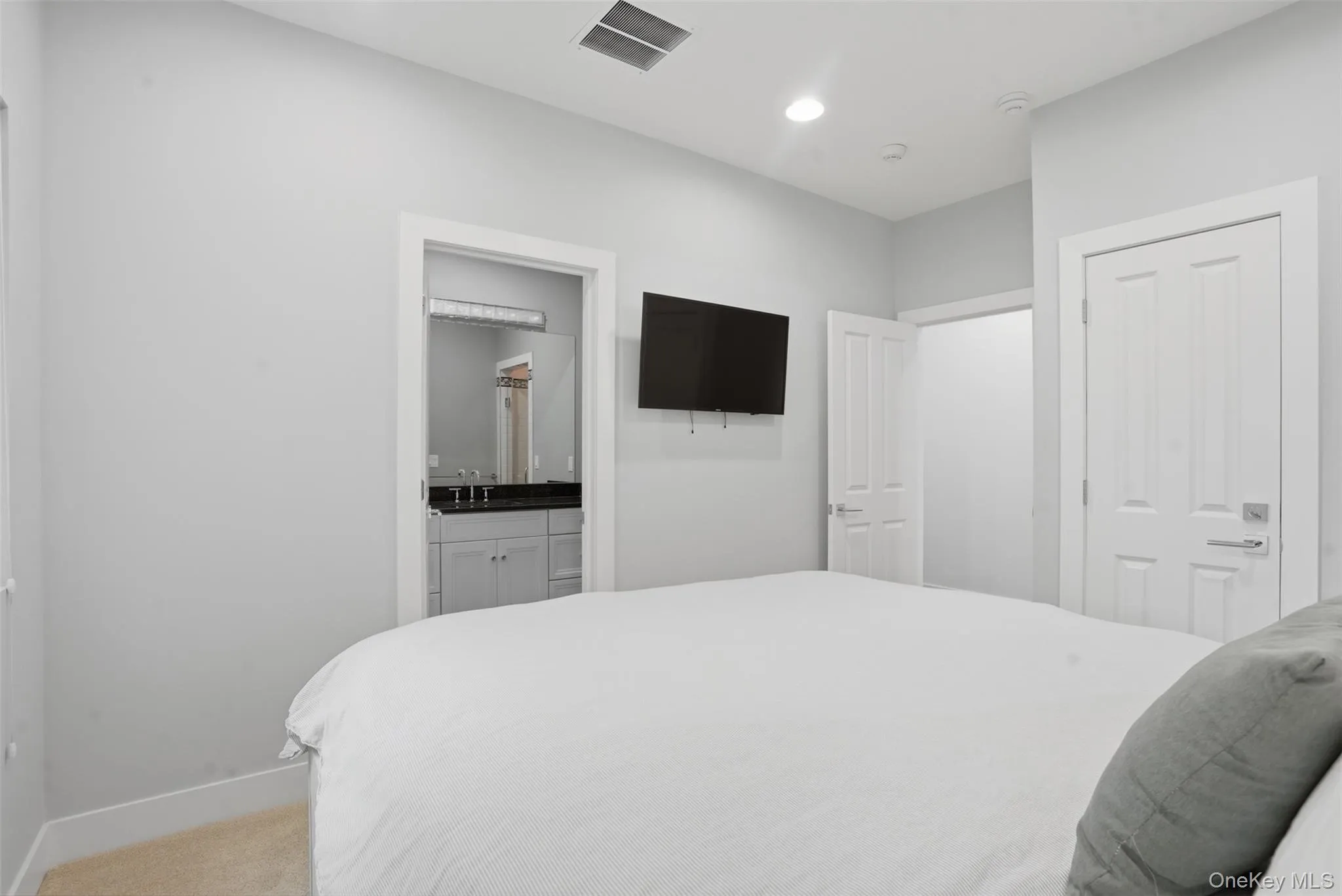 Recessed lighting illuminates the bedroom, featuring light-colored walls and carpet Recessed lighting illuminates the bedroom, featuring light-colored walls and carpet