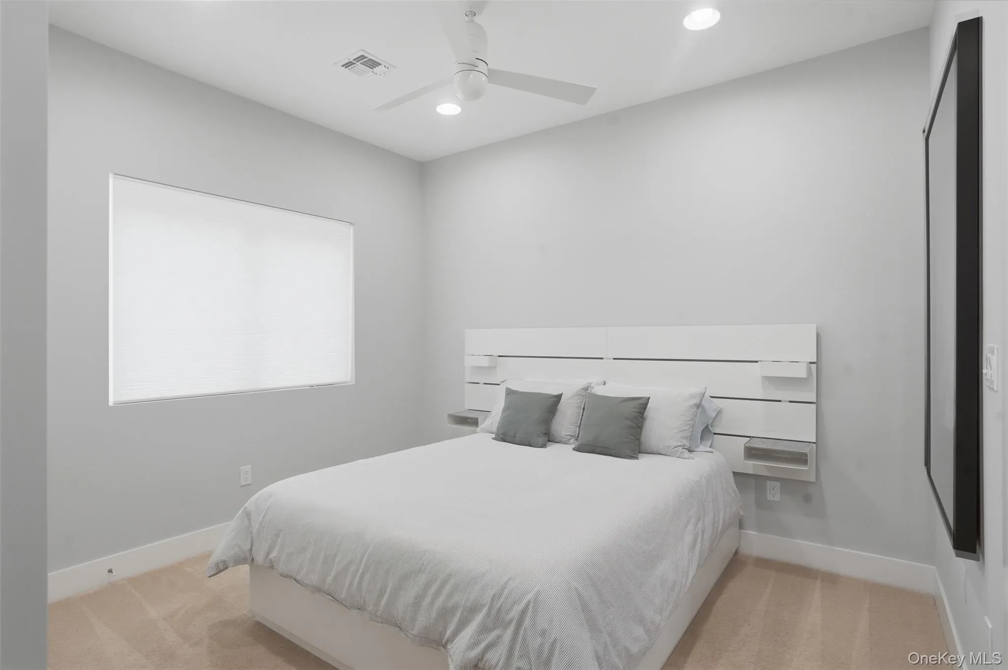 Spacious room featuring neutral paint tones, recessed lighting, a modern ceiling fan, a large window with roller shades, and plush carpeting Spacious room featuring neutral paint tones, recessed lighting, a modern ceiling fan, a large window with roller shades, and plush carpeting