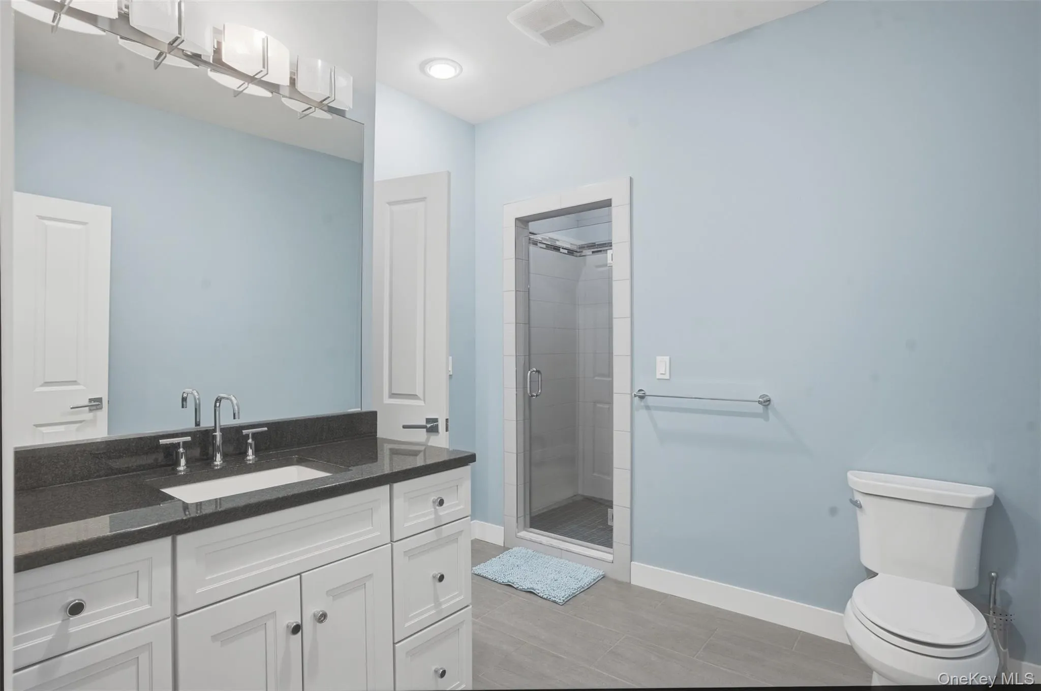 Bathroom featuring a white vanity with a dark stone countertop and an undermount sink Bathroom featuring a white vanity with a dark stone countertop and an undermount sink