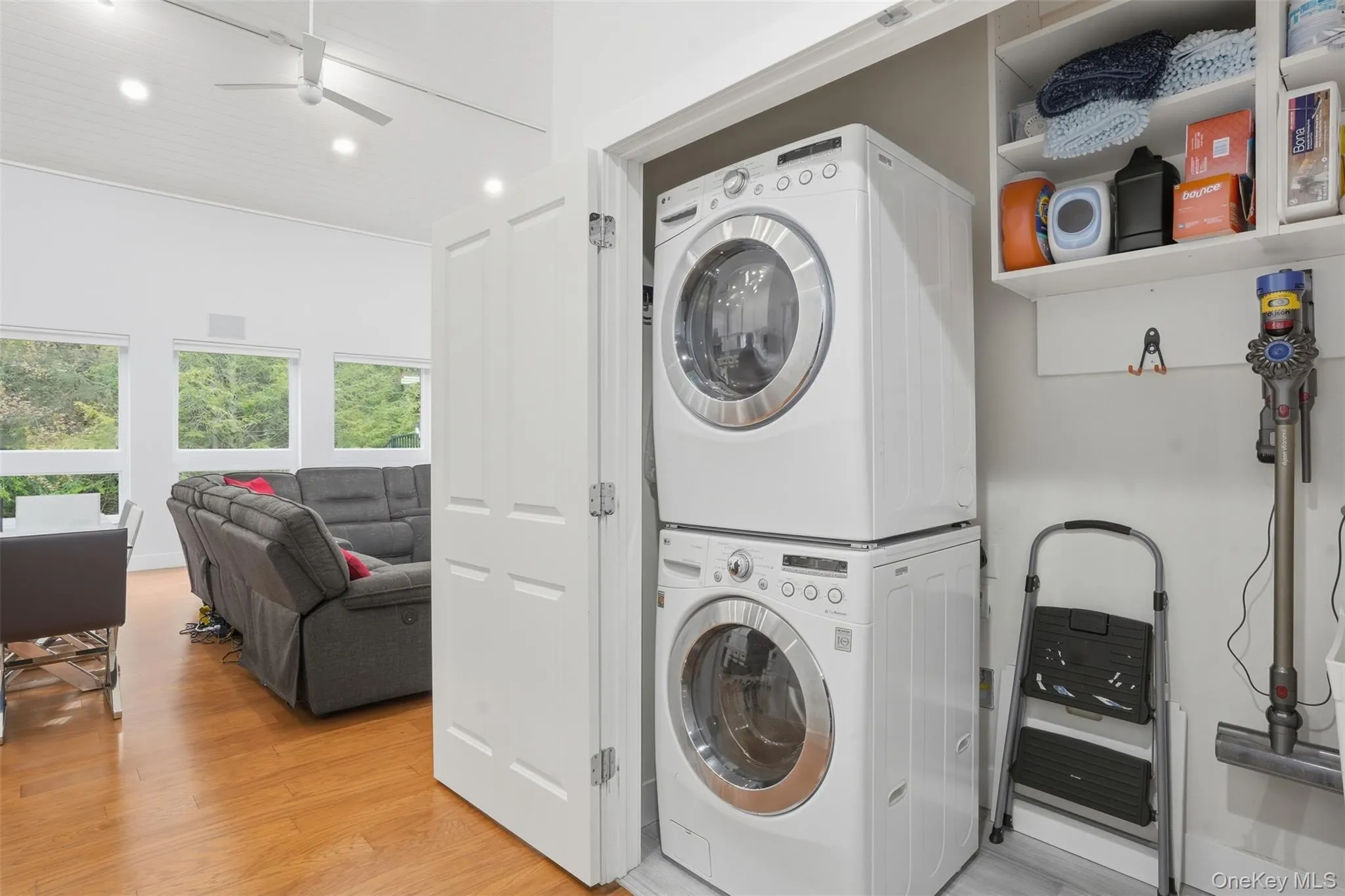 Dedicated laundry closet featuring a stacked washer and dryer, adjacent to an open-concept living space with multiple windows, recessed lighting, and a ceiling fan Dedicated laundry closet featuring a stacked washer and dryer, adjacent to an open-concept living space with multiple windows, recessed lighting, and a ceiling fan