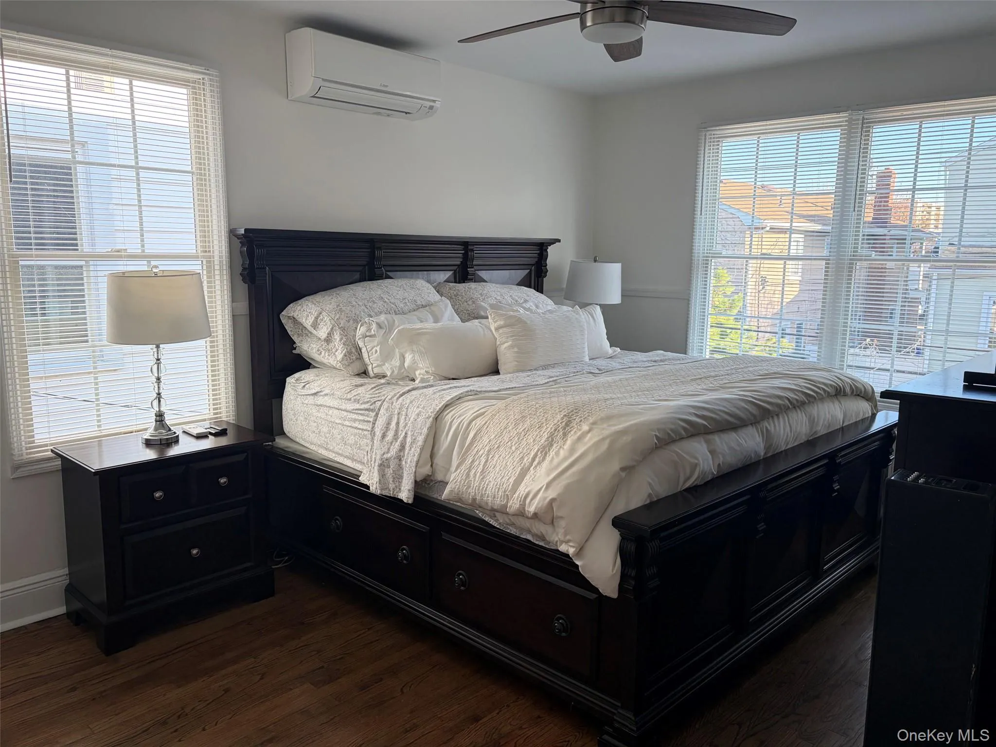 Hardwood-style flooring throughout this room, featuring multiple windows with blinds, a ceiling fan, and a wall-mounted mini-split AC unit and flat screen tv Hardwood-style flooring throughout this room, featuring multiple windows with blinds, a ceiling fan, and a wall-mounted mini-split AC unit and flat screen tv