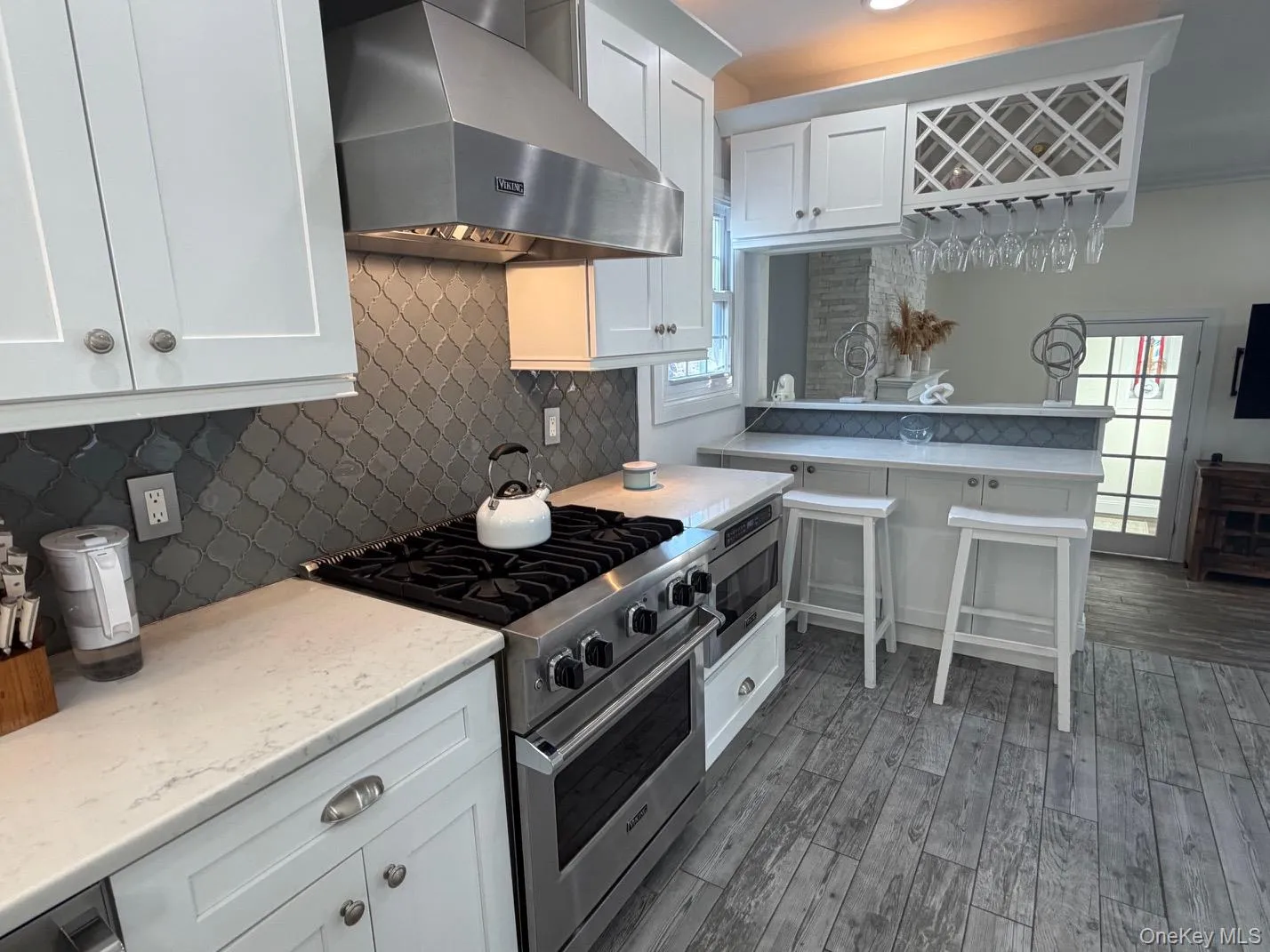 Kitchen featuring stainless steel range with matching vent hood, white shaker cabinetry, light-toned countertops, and a gray arabesque tile backsplash Kitchen featuring stainless steel range with matching vent hood, white shaker cabinetry, light-toned countertops, and a gray arabesque tile backsplash