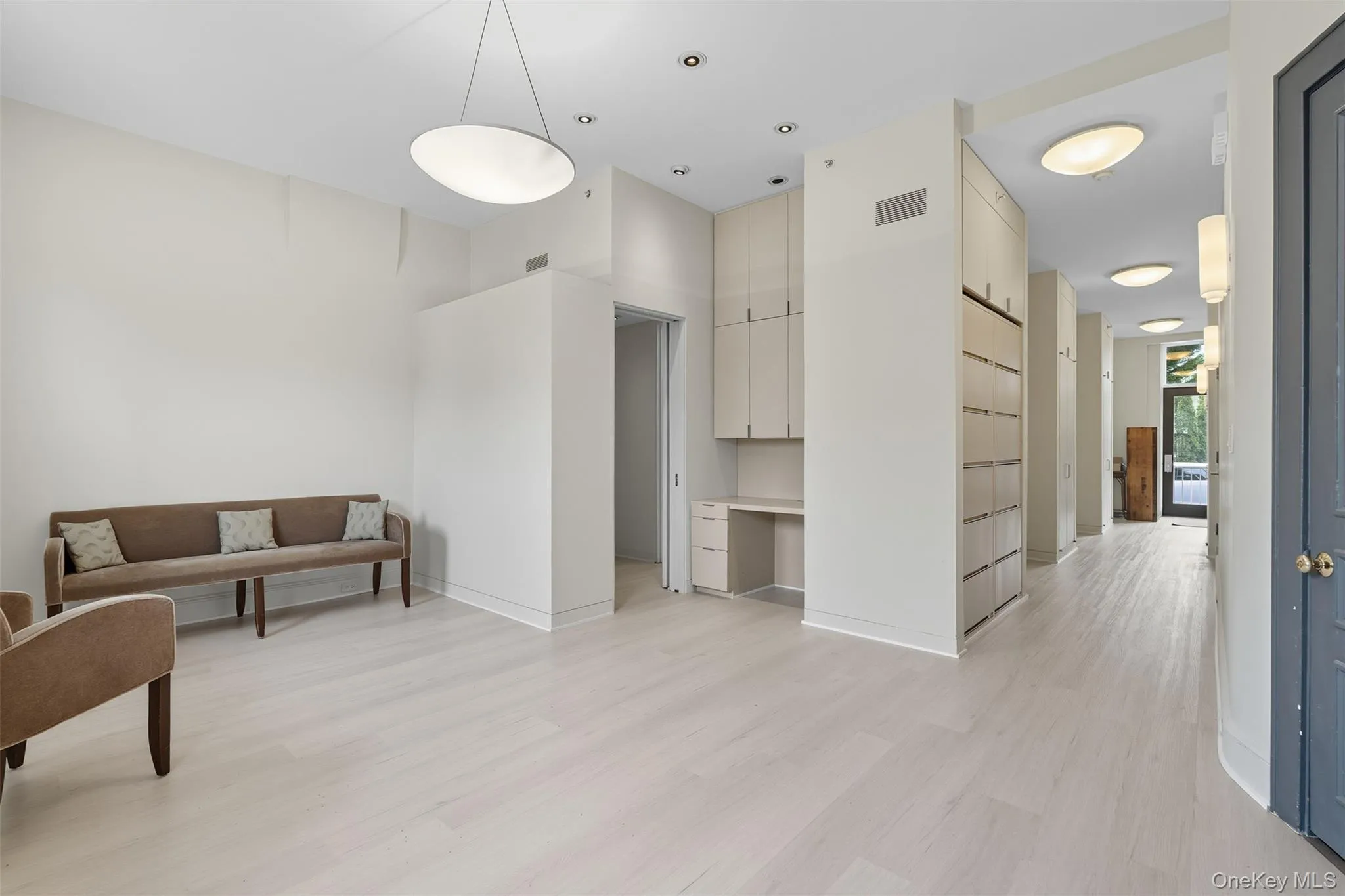 Spacious interior featuring light wood-finish flooring, recessed lighting, a modern pendant light, and integrated cabinetry with a built-in desk Spacious interior featuring light wood-finish flooring, recessed lighting, a modern pendant light, and integrated cabinetry with a built-in desk