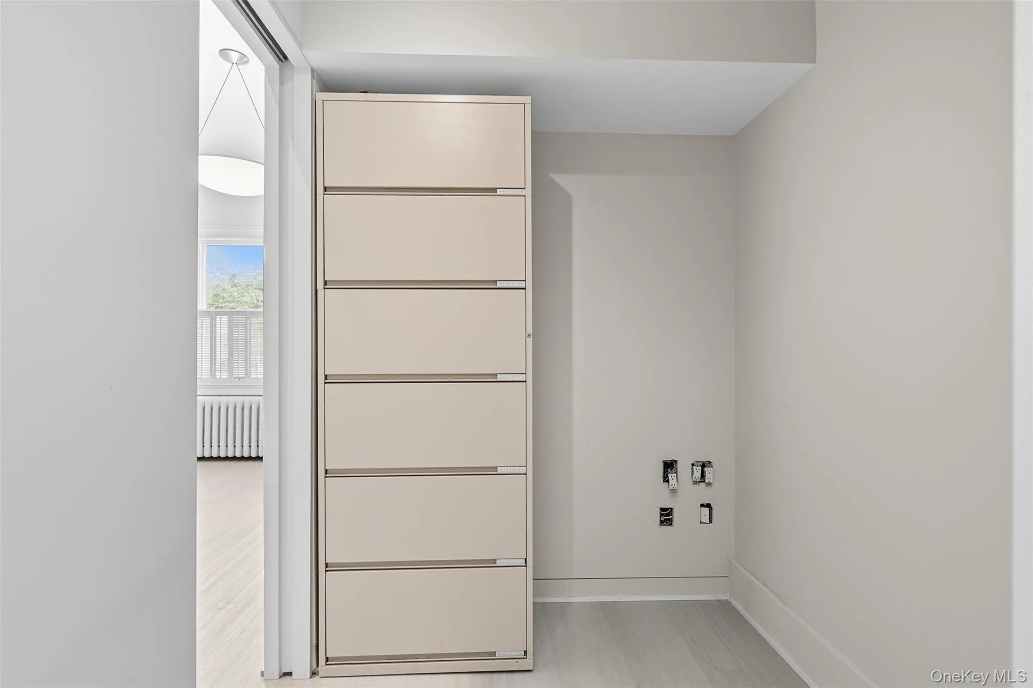 Laundry area featuring light wood-finish flooring, light neutral wall paint, and a six-drawer built-in storage cabinet Laundry area featuring light wood-finish flooring, light neutral wall paint, and a six-drawer built-in storage cabinet