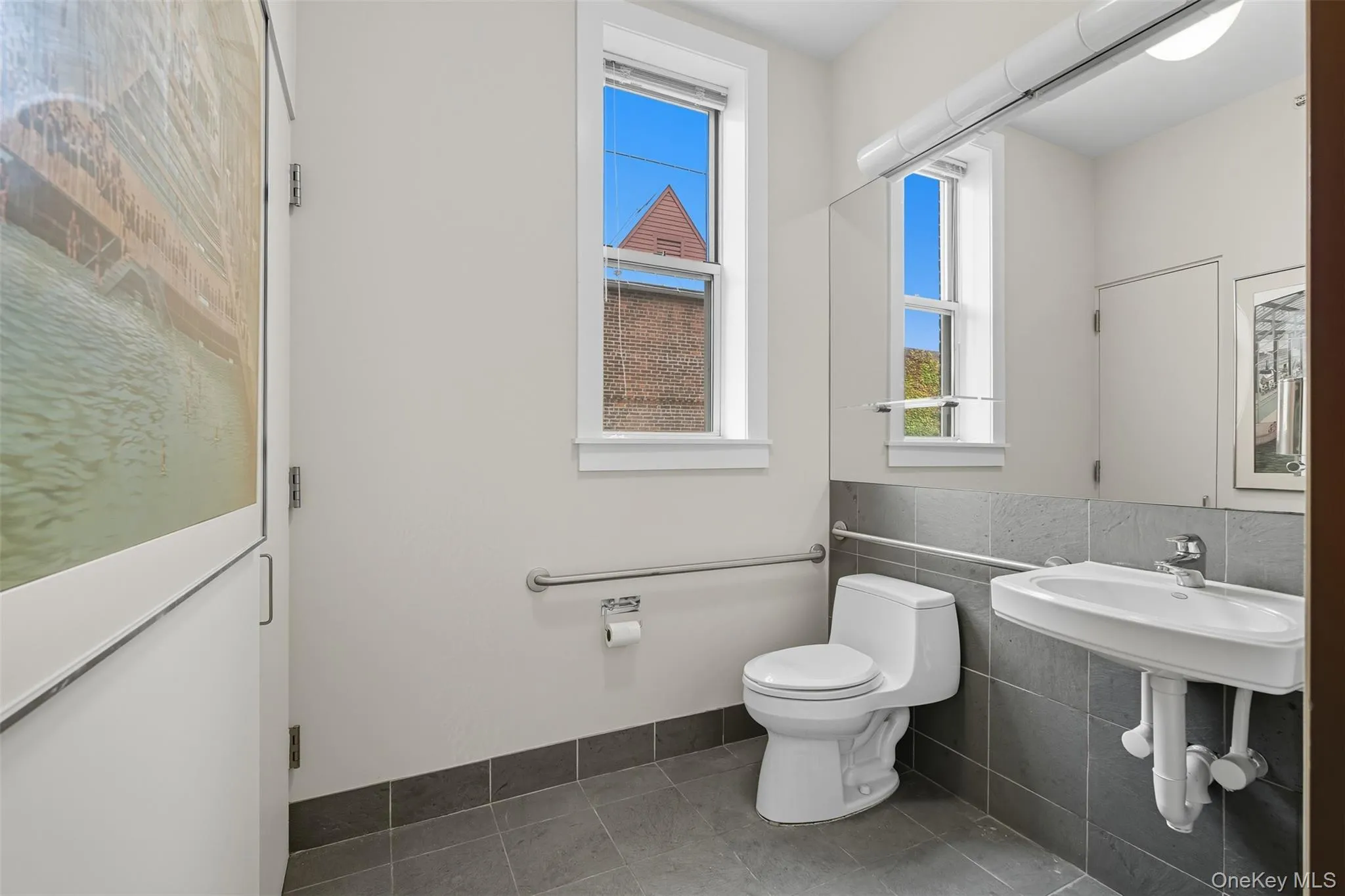 Bathroom featuring a wall-mounted sink, a toilet, and a window with blinds Bathroom featuring a wall-mounted sink, a toilet, and a window with blinds
