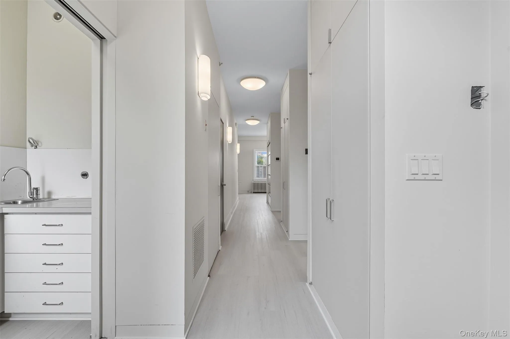 Hallway featuring light wood-finish flooring, recessed ceiling lights, and wall-mounted sconces Hallway featuring light wood-finish flooring, recessed ceiling lights, and wall-mounted sconces
