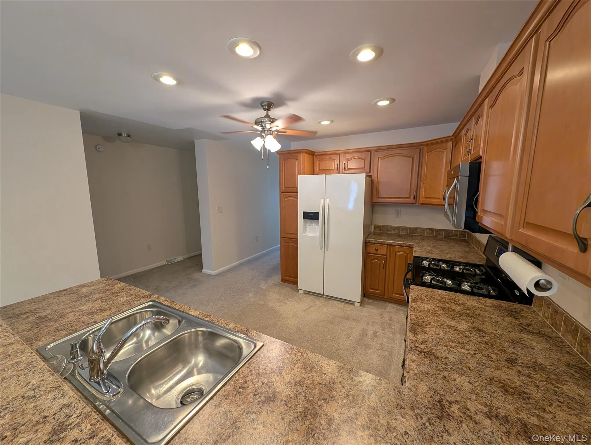 Kitchen featuring light carpet, black range with gas stovetop, ceiling fan, sink, and white fridge with ice dispenser Kitchen featuring light carpet, black range with gas stovetop, ceiling fan, sink, and white fridge with ice dispenser