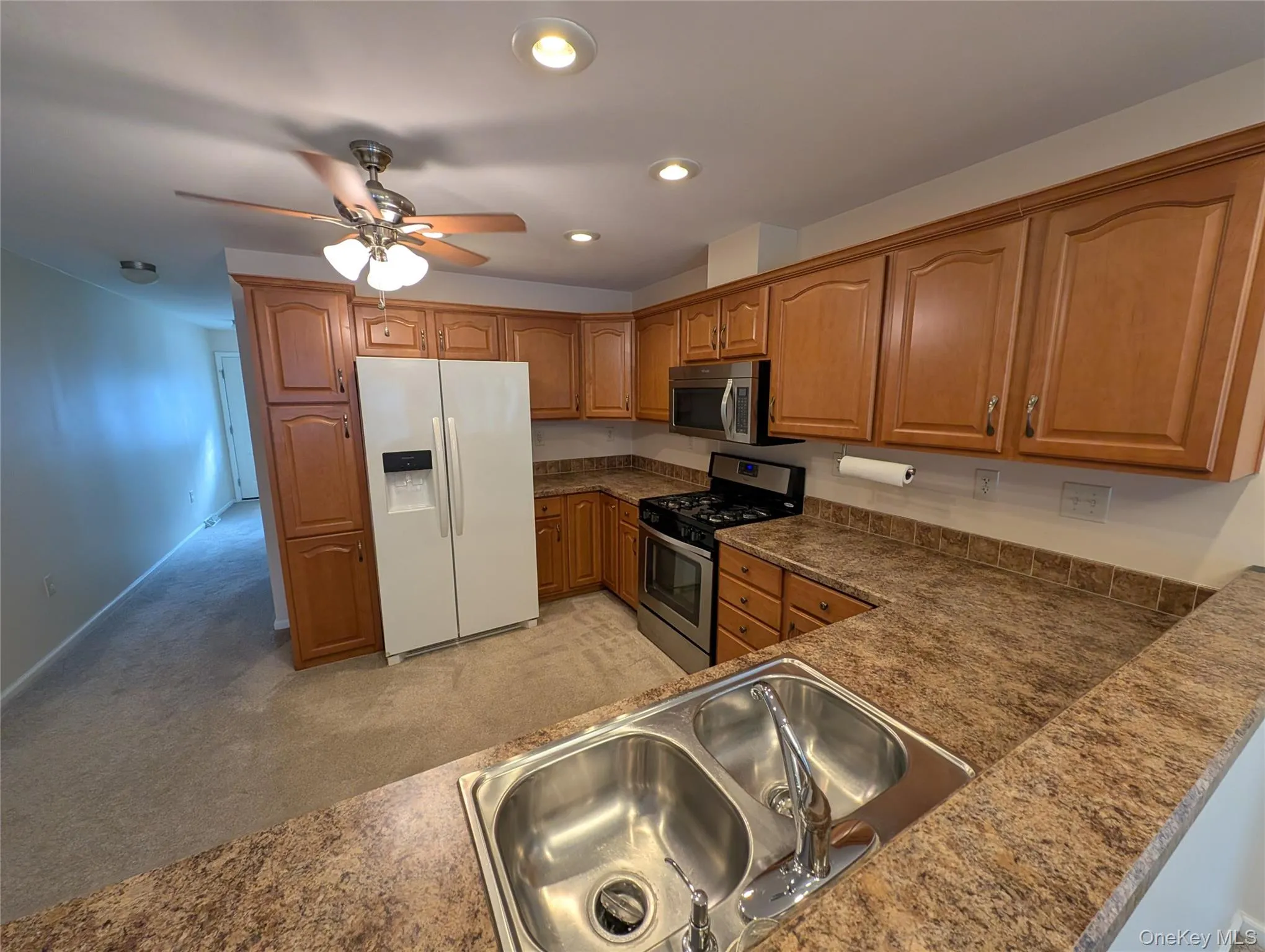Kitchen featuring ceiling fan, light colored carpet, sink, and appliances with stainless steel finishes Kitchen featuring ceiling fan, light colored carpet, sink, and appliances with stainless steel finishes