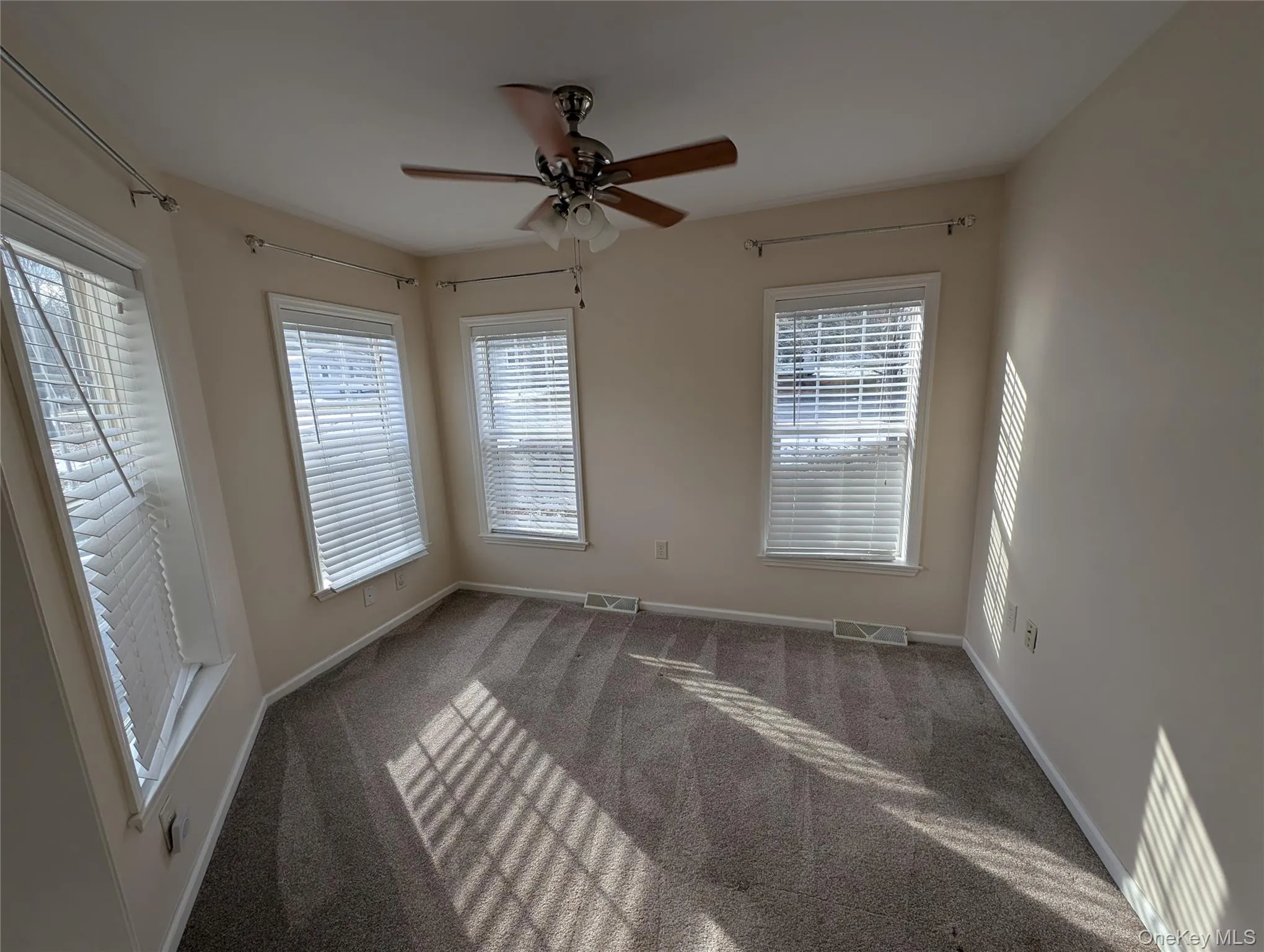 Empty room with ceiling fan, a healthy amount of sunlight, and carpet floors Empty room with ceiling fan, a healthy amount of sunlight, and carpet floors