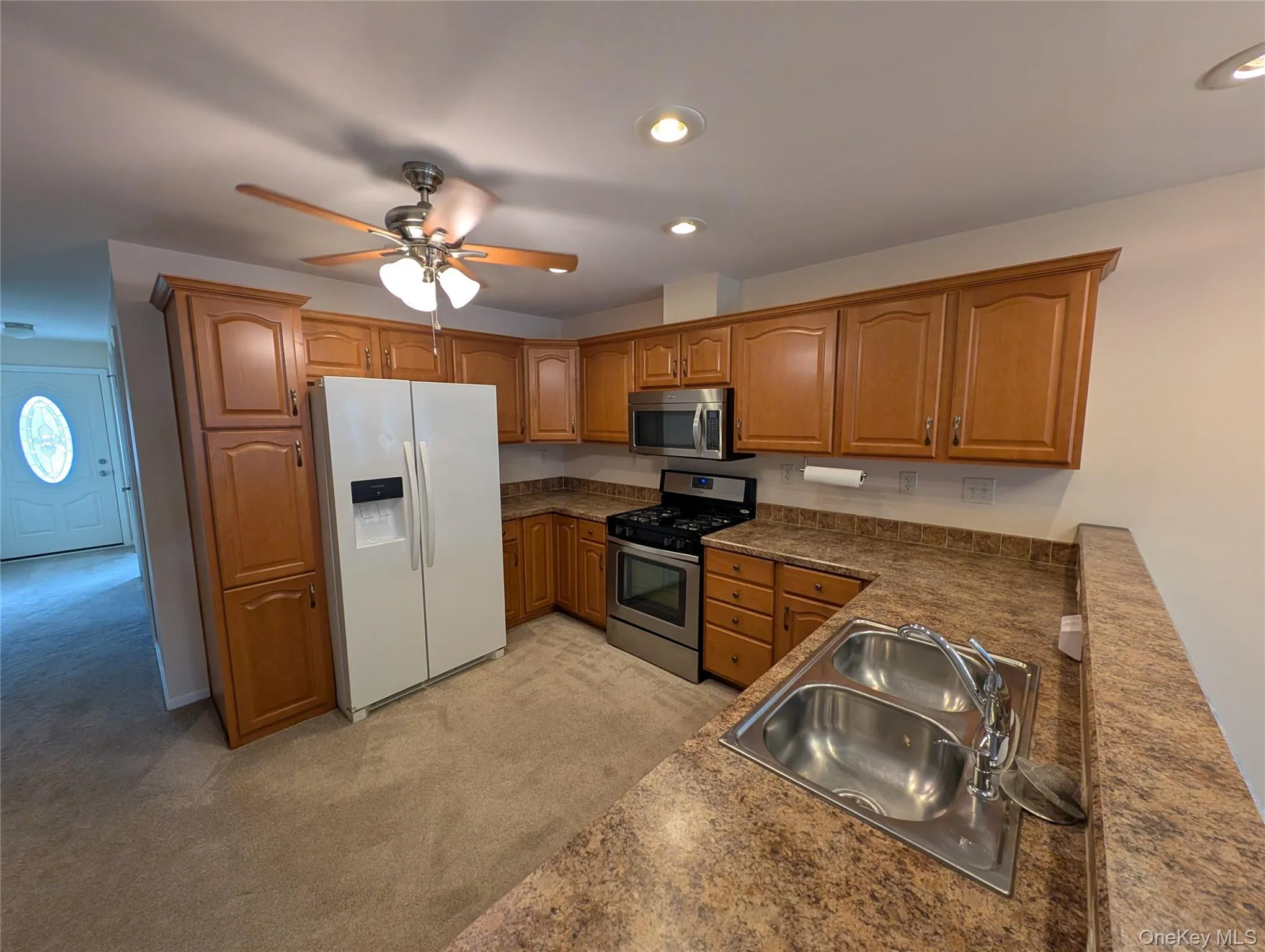 Kitchen featuring ceiling fan, sink, stainless steel appliances, and light carpet Kitchen featuring ceiling fan, sink, stainless steel appliances, and light carpet