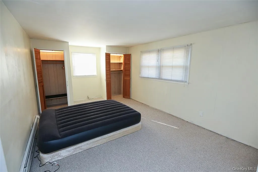 Carpeted room featuring two windows, each with blinds, and two closets with louvered bifold doors Carpeted room featuring two windows, each with blinds, and two closets with louvered bifold doors