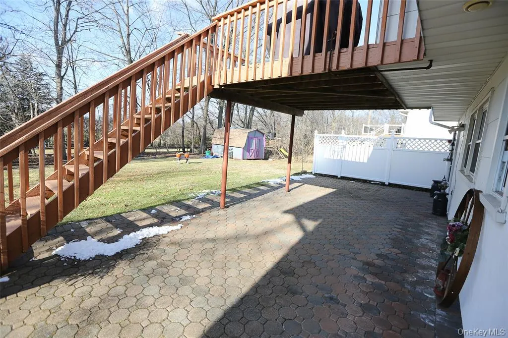 Patio area featuring a patterned paver surface, covered overhead space, and white lattice fencing Patio area featuring a patterned paver surface, covered overhead space, and white lattice fencing