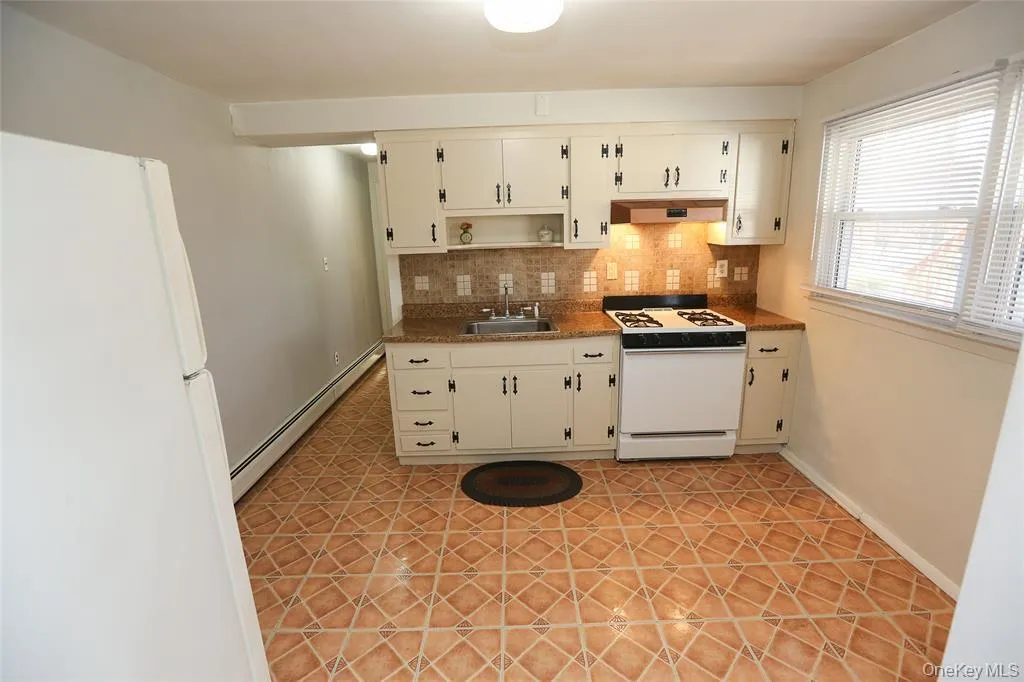 Kitchen featuring light-toned cabinetry with dark hardware, a gas range with an overhead vent, and a stainless steel sink Kitchen featuring light-toned cabinetry with dark hardware, a gas range with an overhead vent, and a stainless steel sink