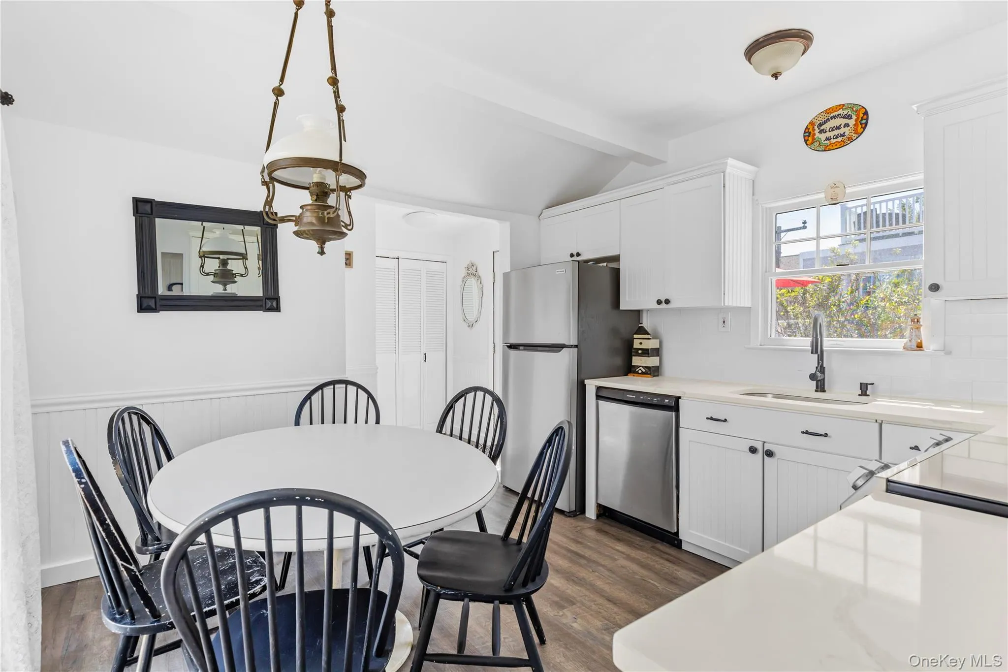 Bright kitchen and dining area featuring white cabinetry, light countertops, stainless steel appliances, and wood-finish flooring Bright kitchen and dining area featuring white cabinetry, light countertops, stainless steel appliances, and wood-finish flooring
