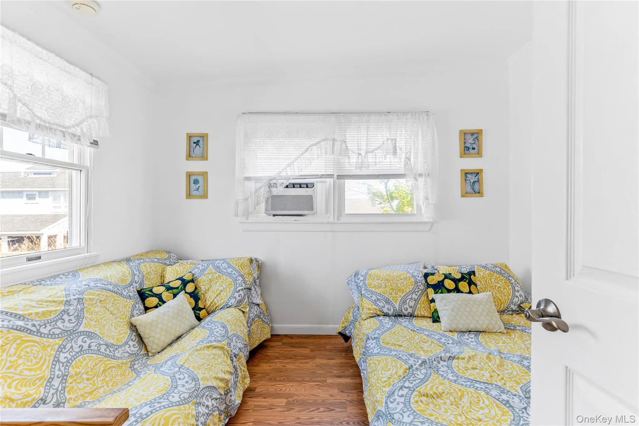 Bright room with a white door, two windows featuring white blinds, and wood-finish flooring Bright room with a white door, two windows featuring white blinds, and wood-finish flooring