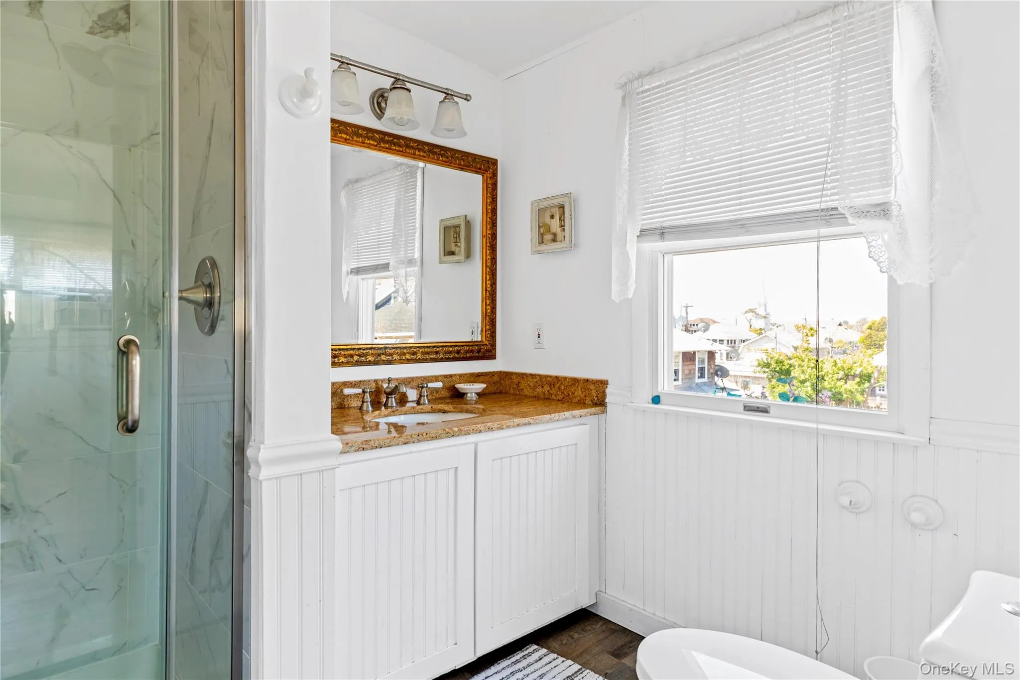 Bathroom featuring a glass-enclosed shower, single vanity with a granite countertop, and white beadboard paneling Bathroom featuring a glass-enclosed shower, single vanity with a granite countertop, and white beadboard paneling