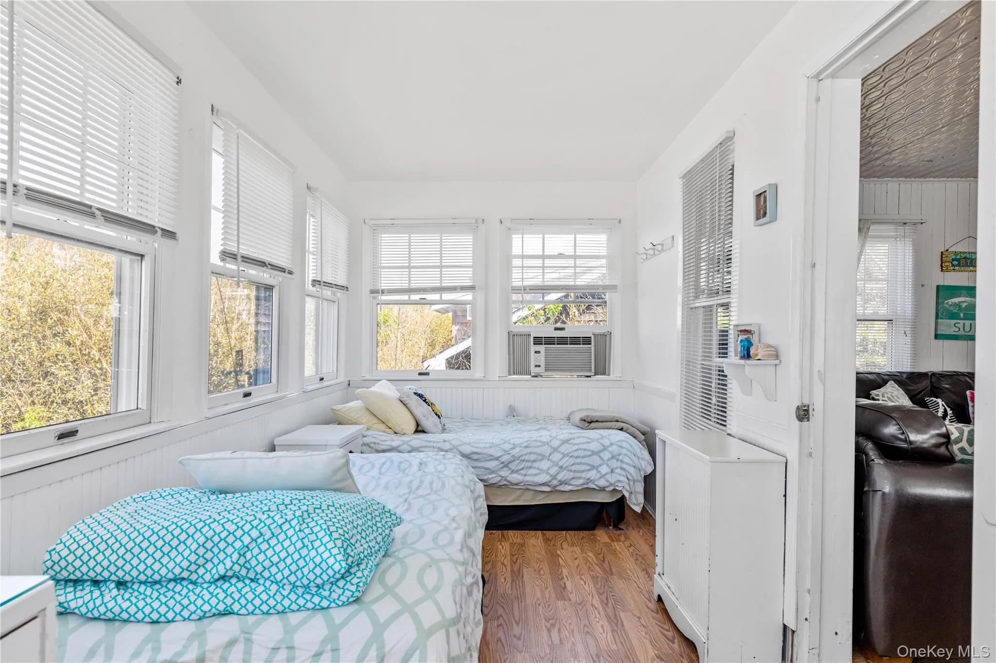 Sunroom featuring multiple windows with blinds, white wall paneling, wood-finish flooring, and an in-wall air conditioning unit Sunroom featuring multiple windows with blinds, white wall paneling, wood-finish flooring, and an in-wall air conditioning unit