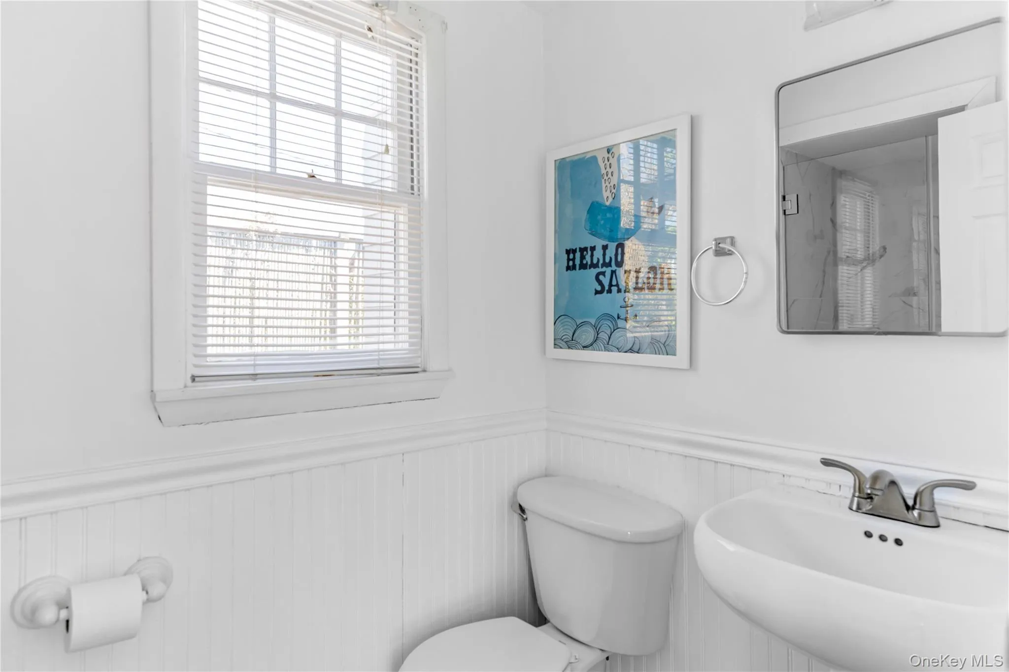 Bathroom featuring wainscoting, an integrated wall-mount sink, two-handle faucet, a window with blinds, and a mirrored medicine cabinet Bathroom featuring wainscoting, an integrated wall-mount sink, two-handle faucet, a window with blinds, and a mirrored medicine cabinet