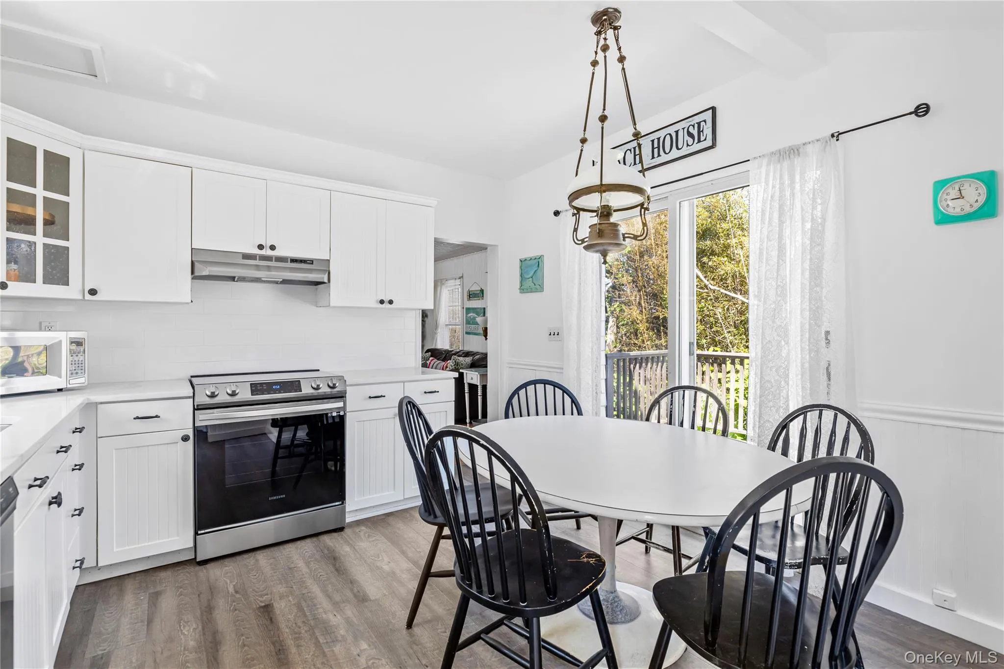 Kitchen and dining area featuring white cabinetry, a white subway tile backsplash, stainless steel range, and wood-finish flooring Kitchen and dining area featuring white cabinetry, a white subway tile backsplash, stainless steel range, and wood-finish flooring