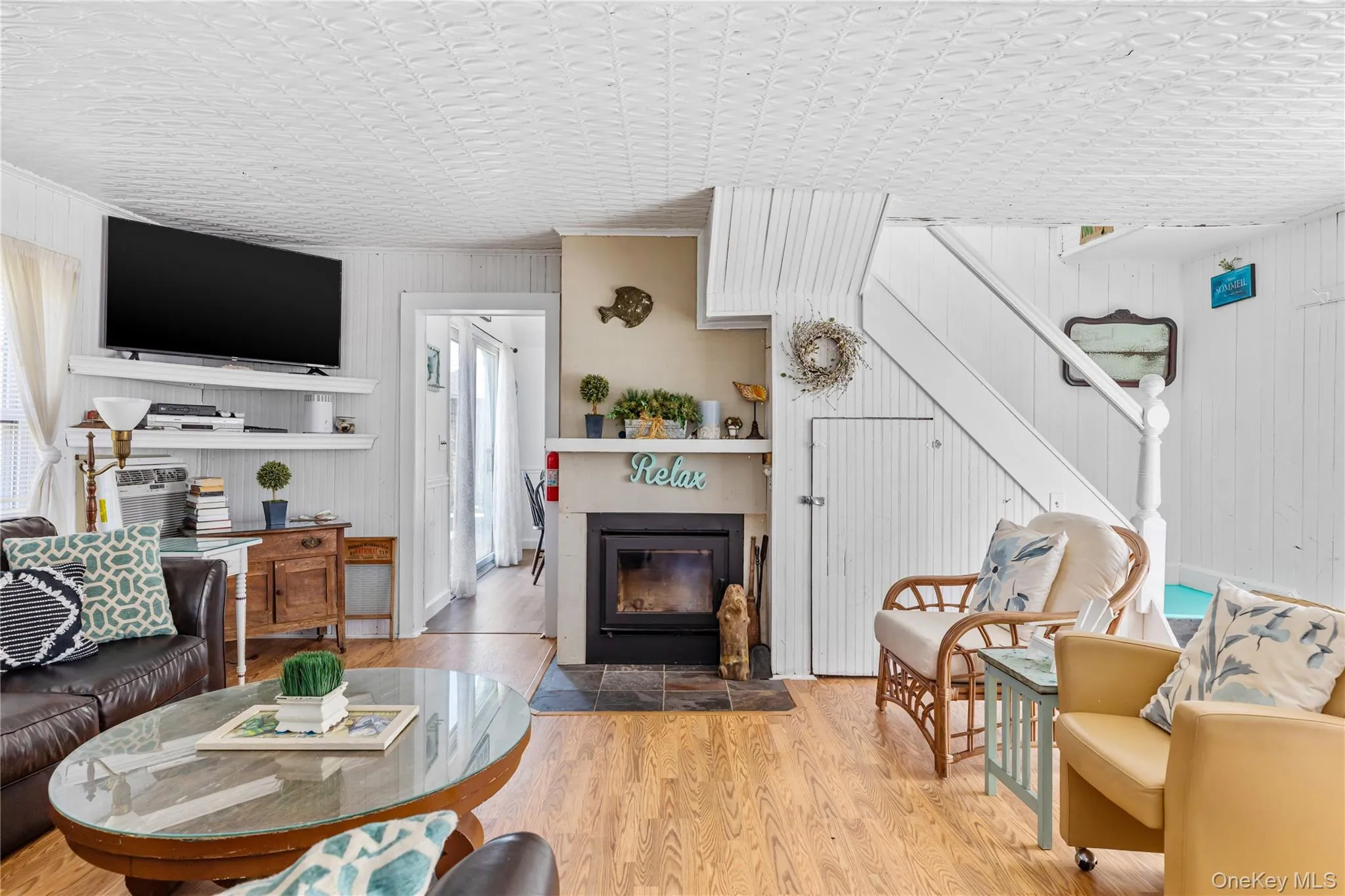 Living area featuring wood-finish flooring, a fireplace with a stone hearth, white shiplap walls, a white staircase with a paneled base, and a paneled ceiling Living area featuring wood-finish flooring, a fireplace with a stone hearth, white shiplap walls, a white staircase with a paneled base, and a paneled ceiling