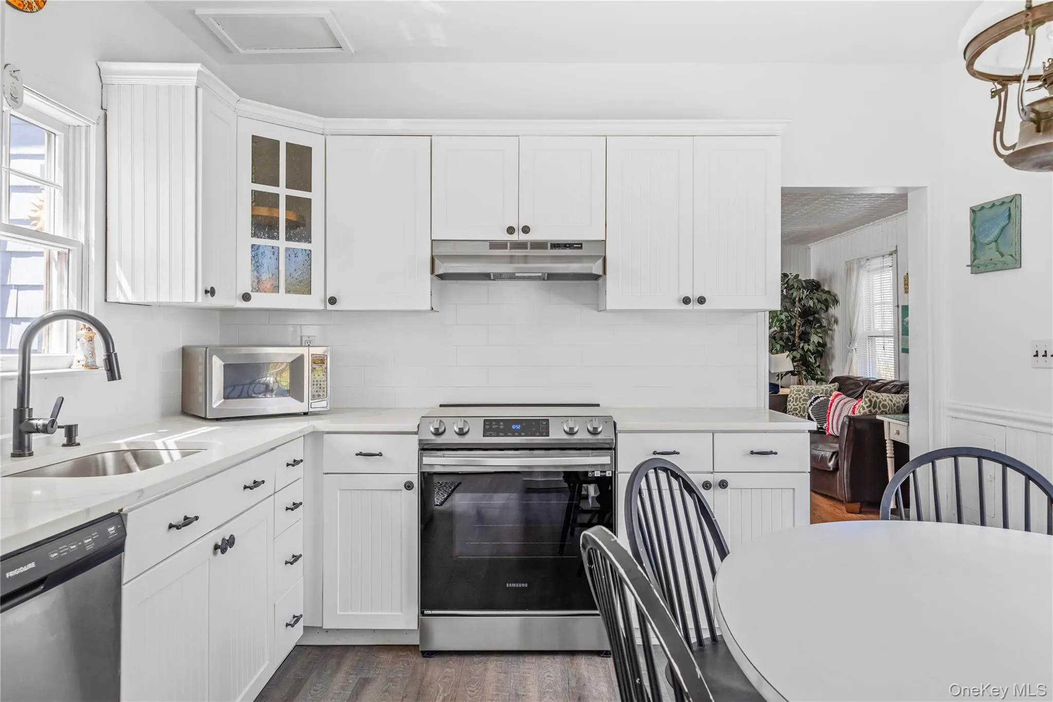 Light-filled kitchen featuring white cabinetry, a stainless steel electric range, a stainless steel dishwasher, a single basin sink with a matte black faucet, and wood-finish flooring Light-filled kitchen featuring white cabinetry, a stainless steel electric range, a stainless steel dishwasher, a single basin sink with a matte black faucet, and wood-finish flooring
