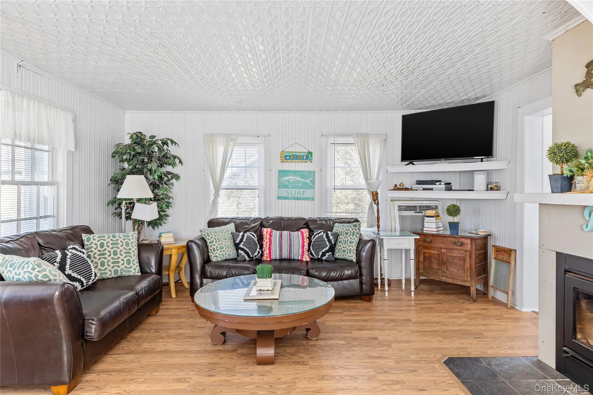 Spacious living area featuring wood-finish flooring, white beadboard walls, and a patterned ceiling Spacious living area featuring wood-finish flooring, white beadboard walls, and a patterned ceiling